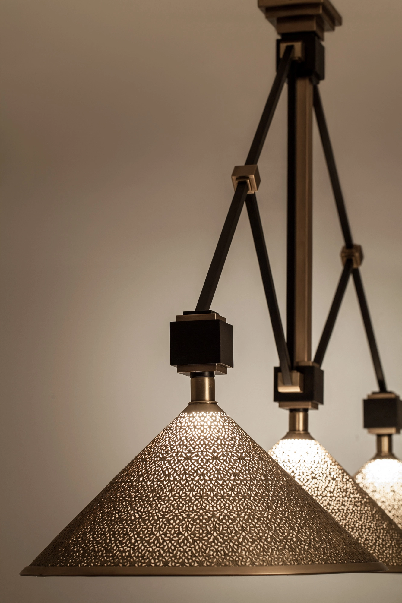 Several conical pierced brass pendant shades seen from below, lit warmly along a rod frame.