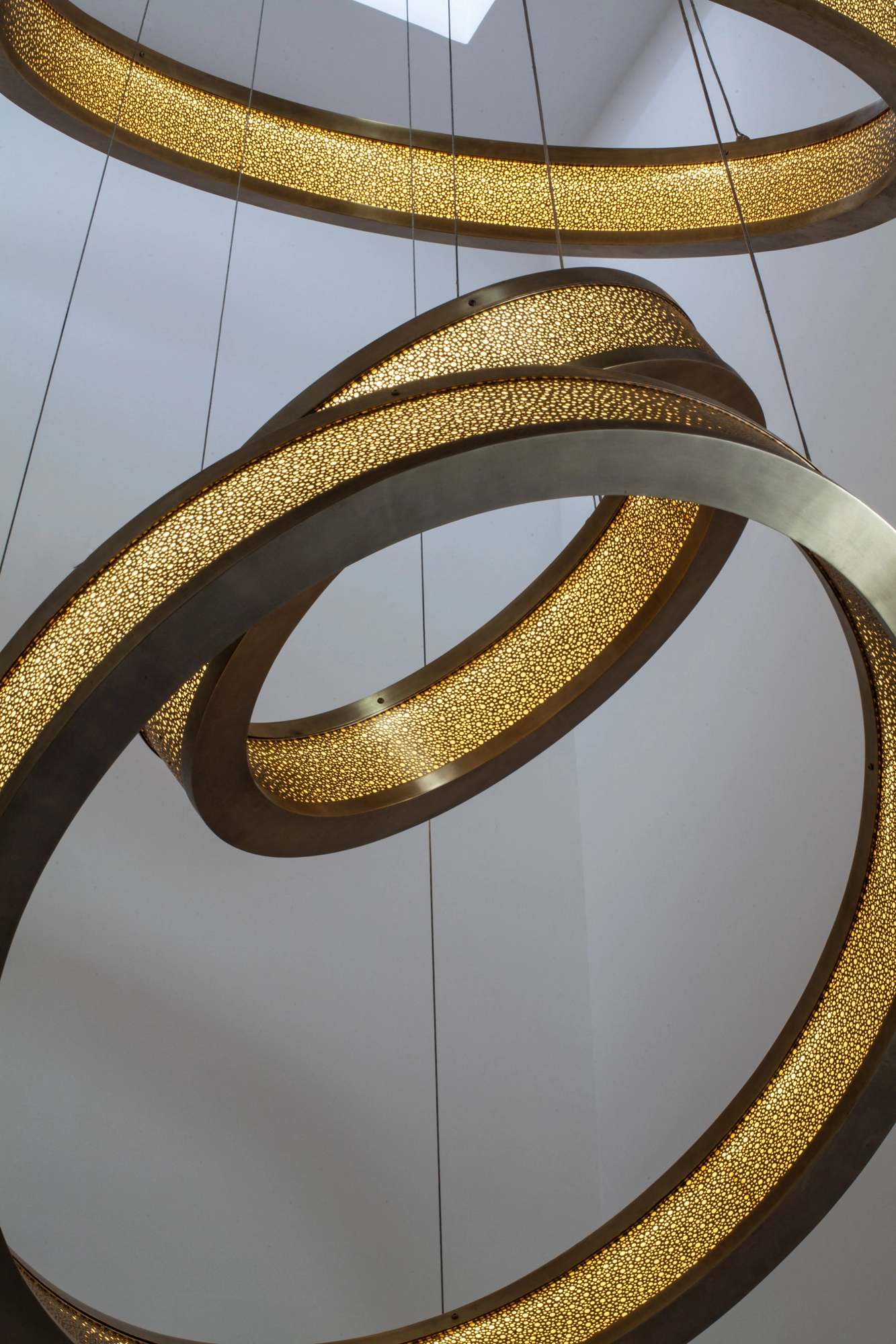 Overlapping gold liquid-light rings of a chandelier seen from below against a white ceiling.