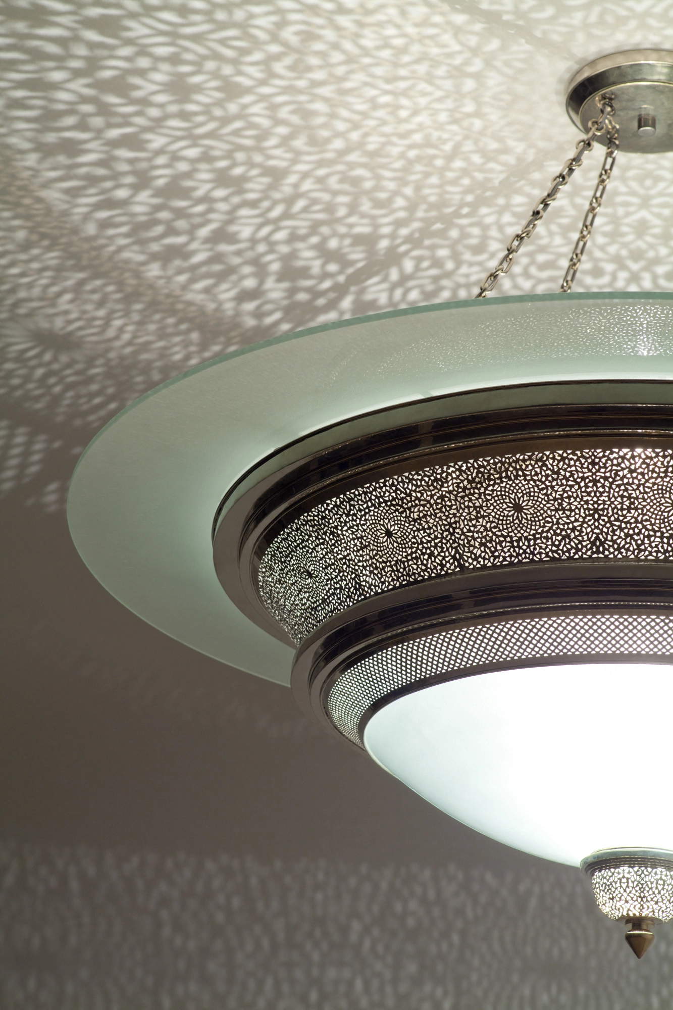 Tiered frosted-glass disc-dome flush ceiling light with pierced brass trim, beneath a dappled light pattern.