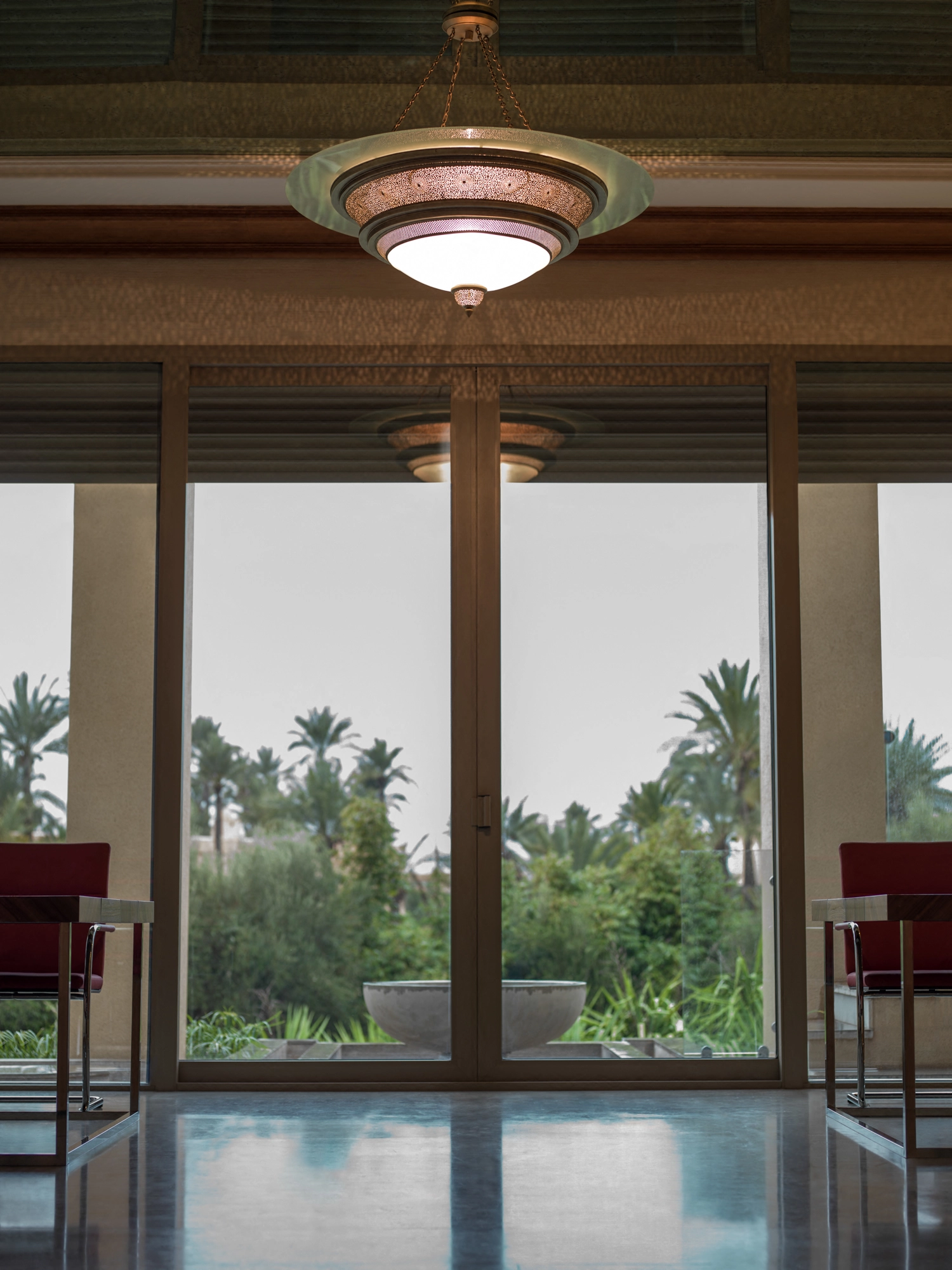 Pierced disc-dome ceiling light above a window overlooking palms and a pool.