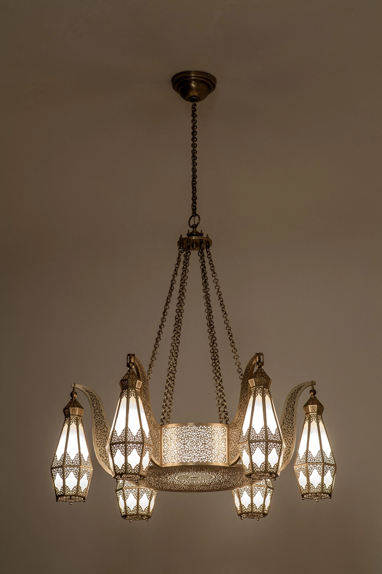 A brass chandelier with a ring of hanging pierced lantern shades on chains, glowing warmly from the ceiling.