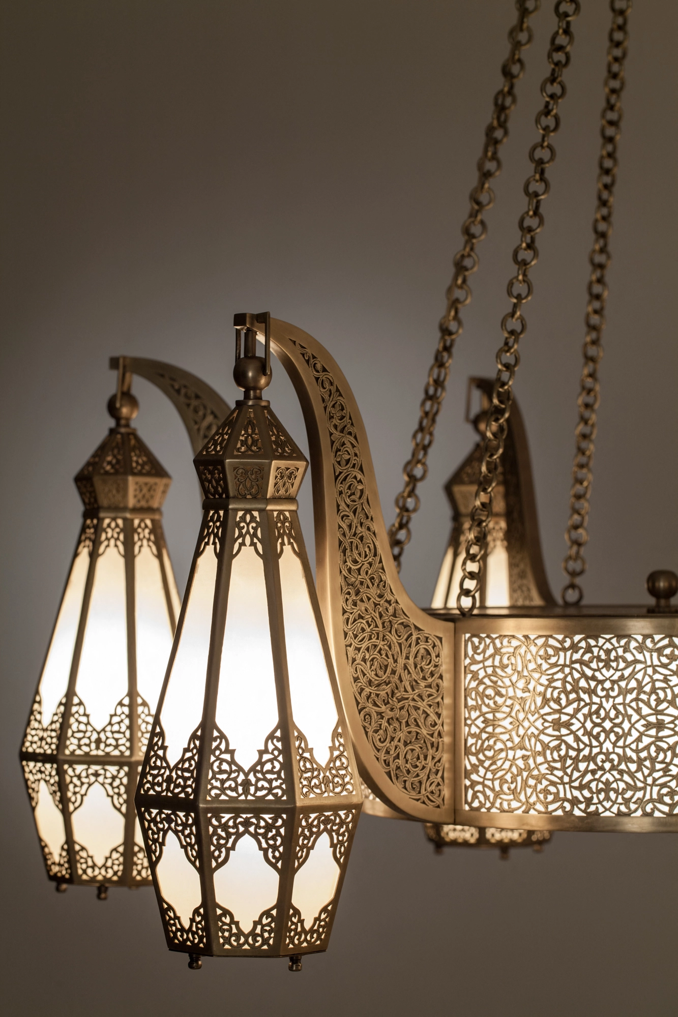 Close-up of a brass chandelier's pierced lantern shades with pale glass panels, glowing warmly.