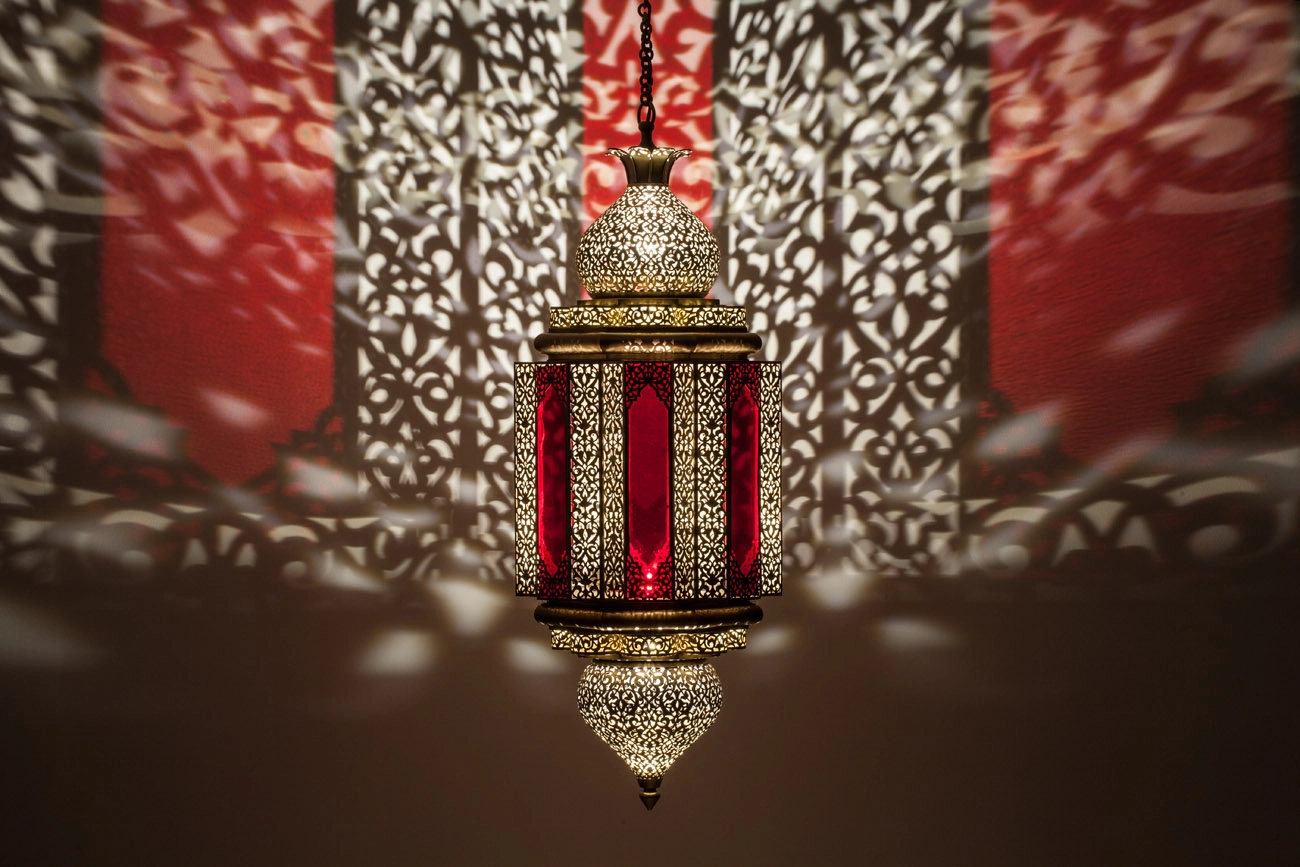 Moorish lantern with red stained-glass panels glowing in a dim room, mirrored in a reflective floor below.
