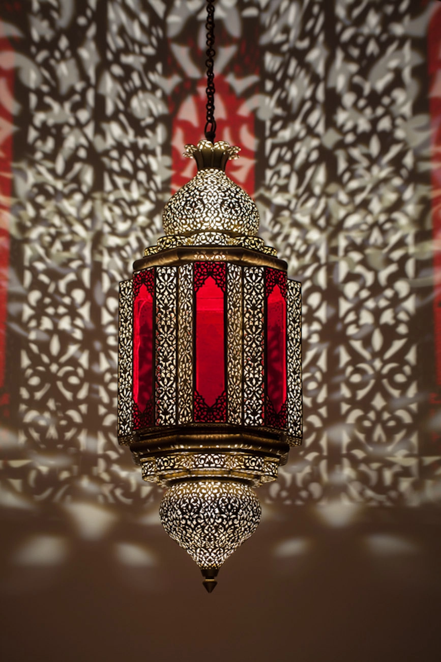 Ornate Moorish lantern with glowing red stained-glass panels and pierced brass, casting a lacy light pattern.