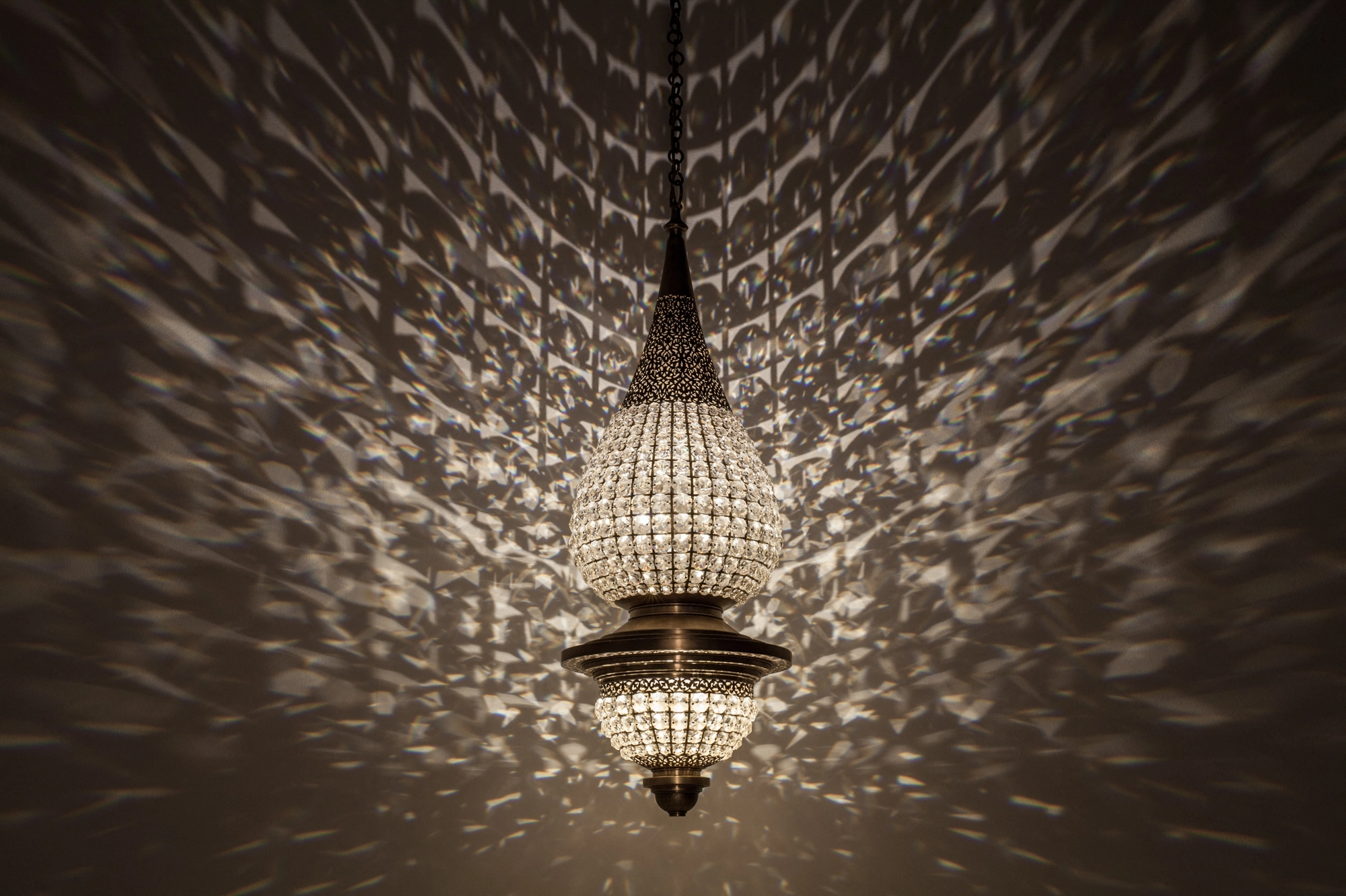 Small crystal pendant chandelier glowing in a dark room, casting a broad scatter of light across the ceiling.