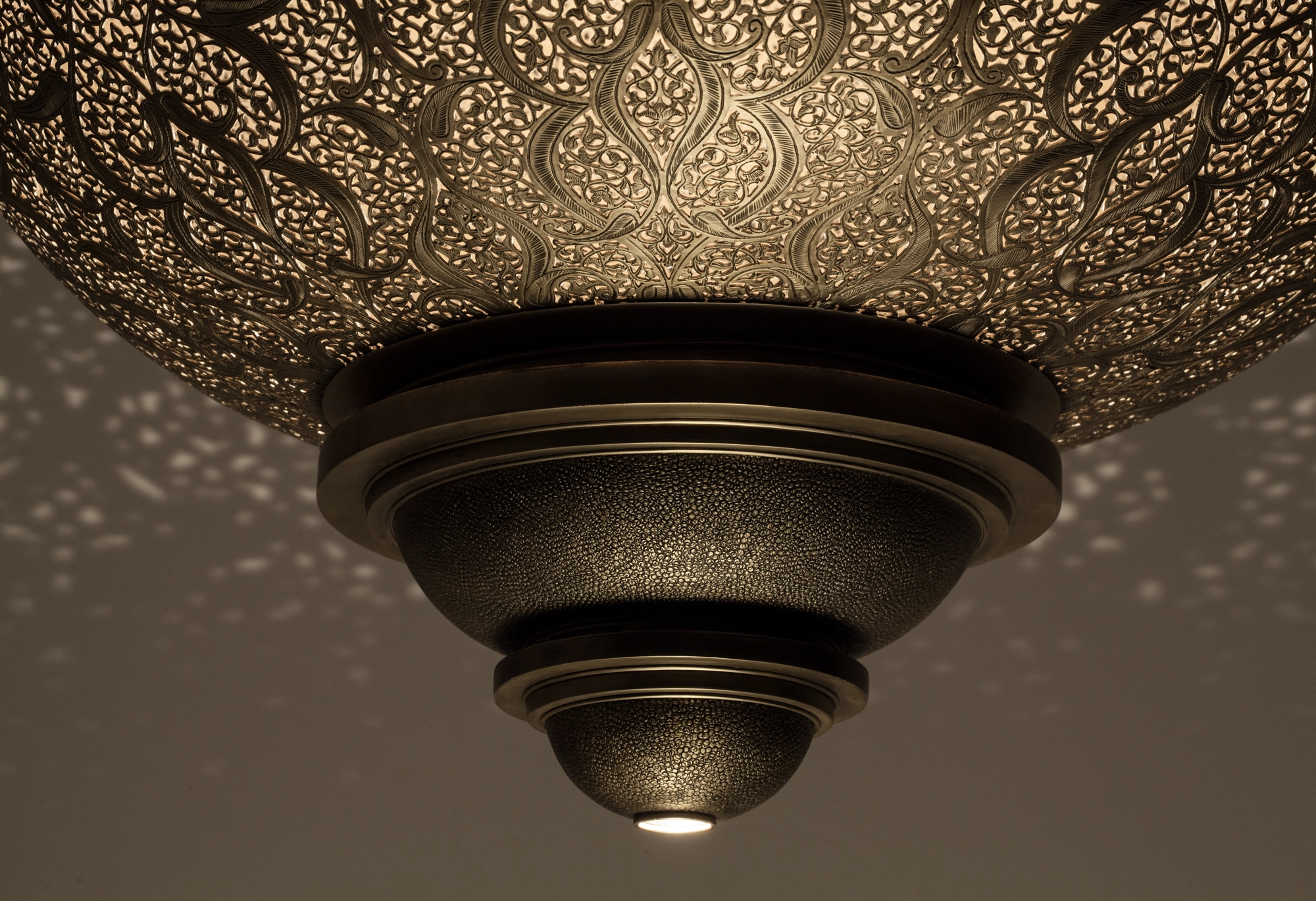 Pierced-brass double-hat globe ceiling fixture glowing beneath a fine halo of projected light dots.
