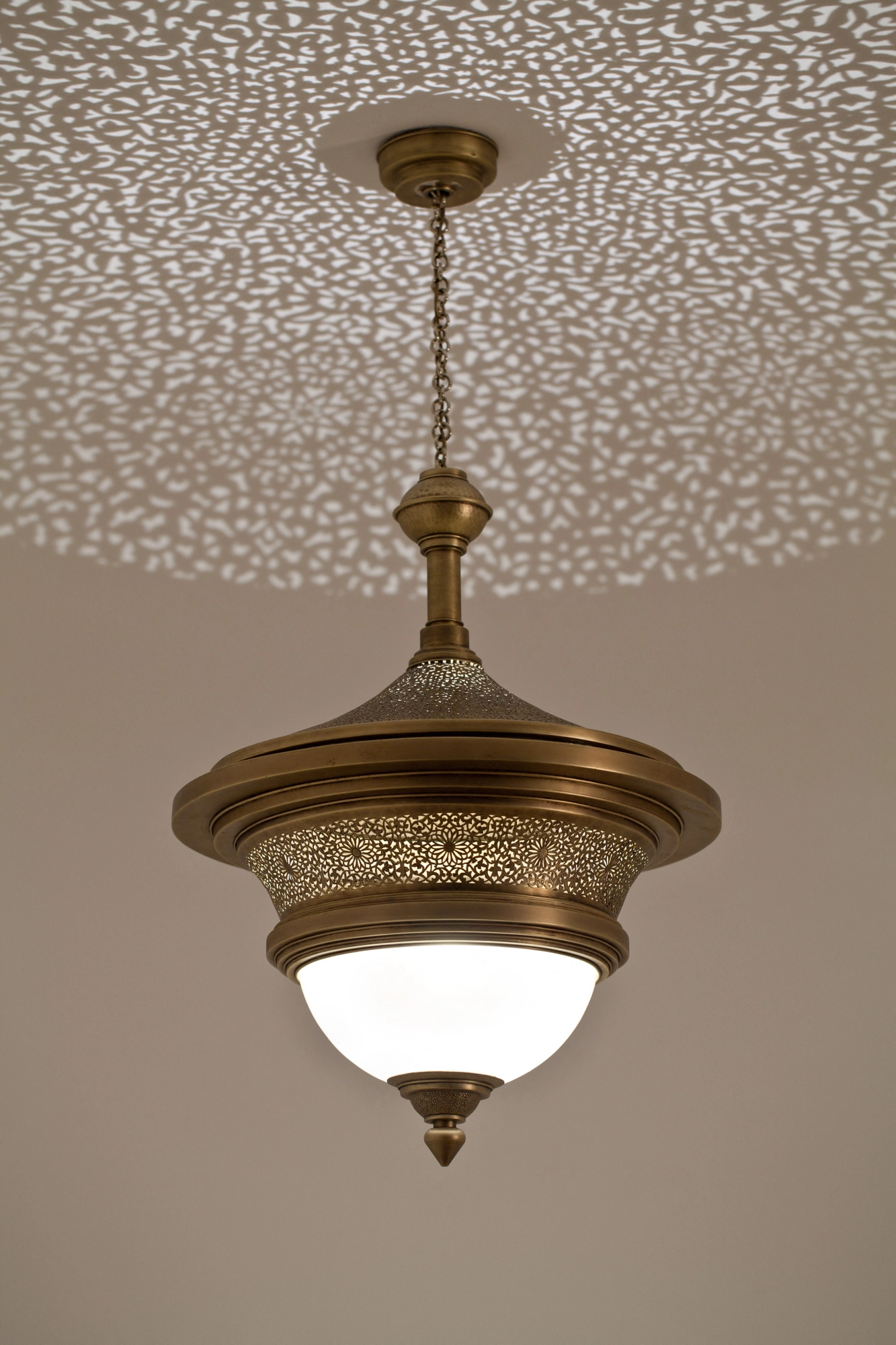 Pendant lamp with stacked pierced-brass tiers above a white glass cloche, hung from a dotted-light ceiling.