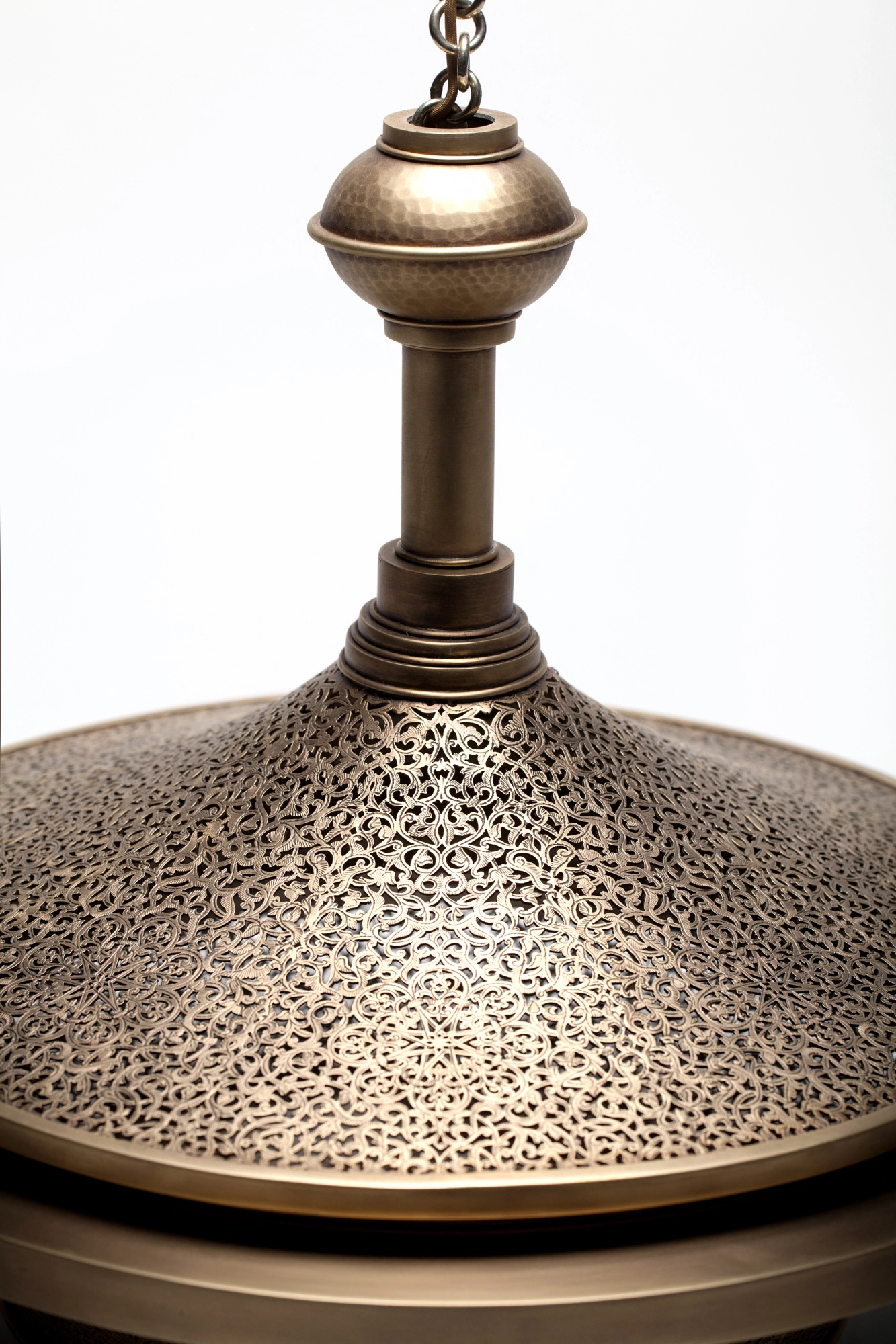 Close-up of the pierced-brass conical top of a cloche pendant, its fine perforations catching warm light.