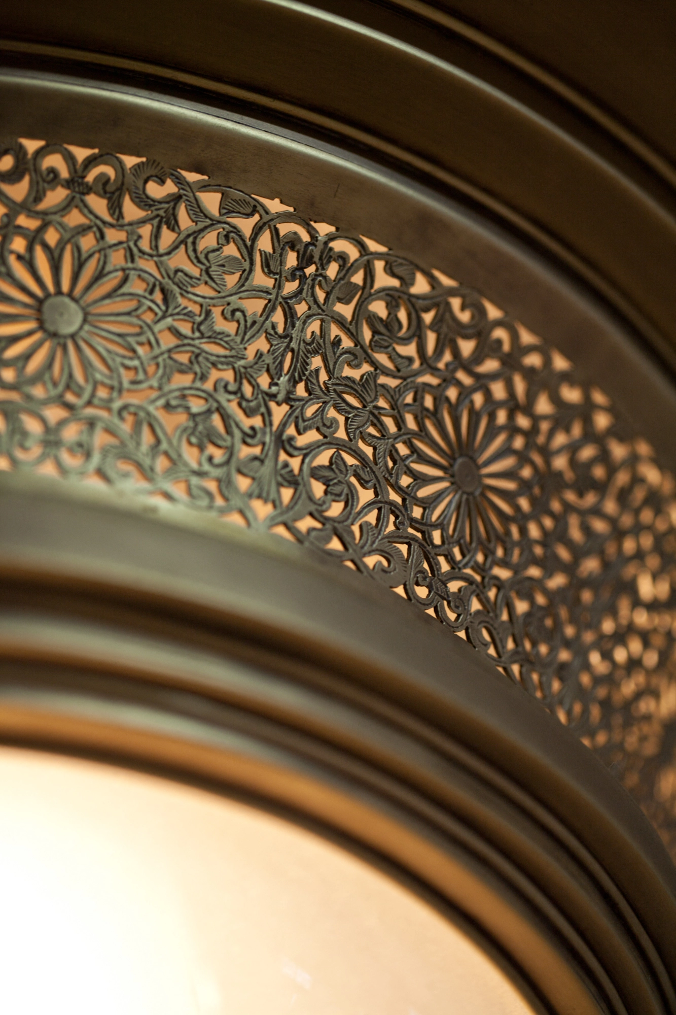 Detail of a pierced-brass pendant rim showing a glowing floral medallion motif against shadow.