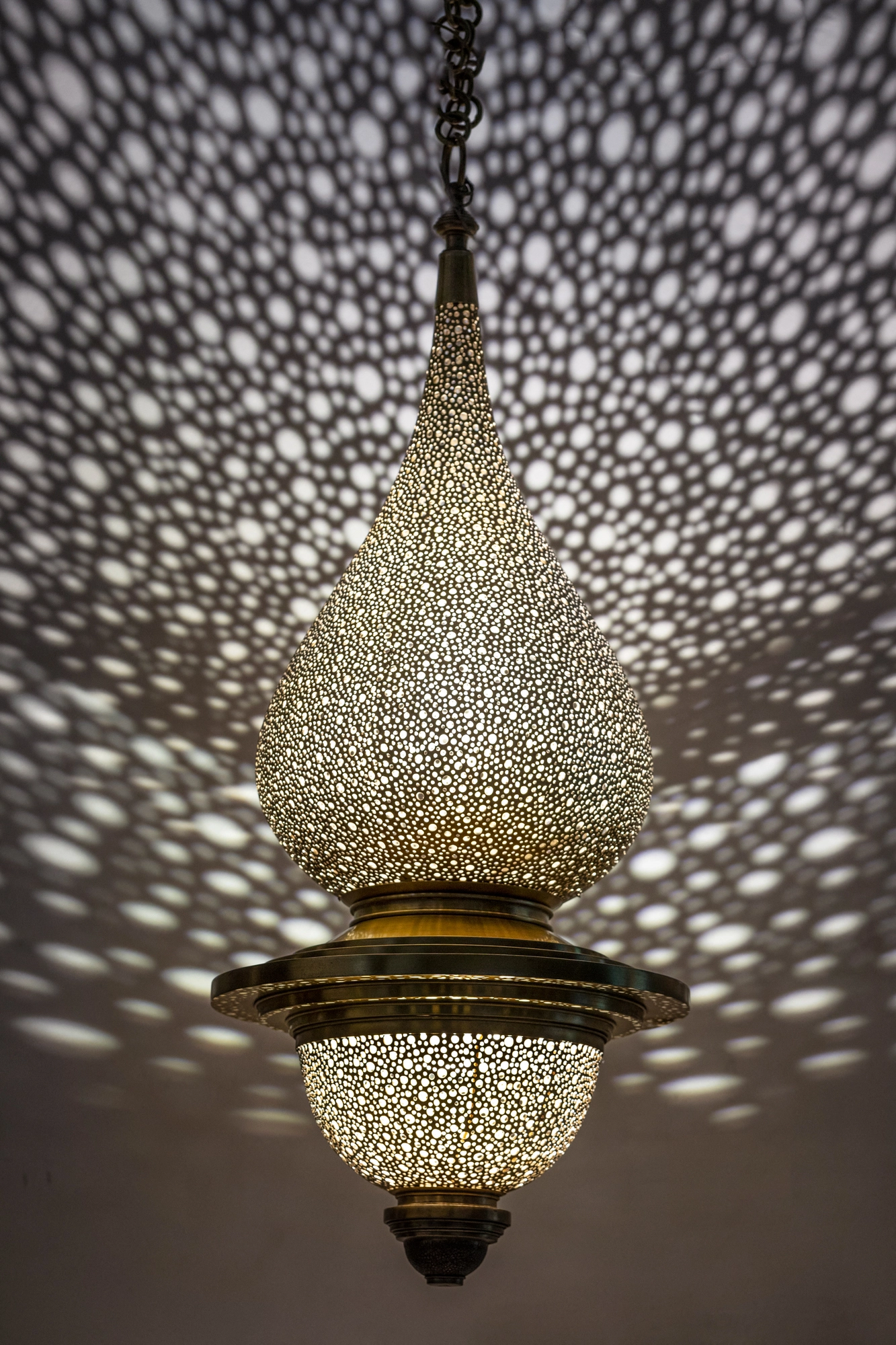 A pierced onion-shaped pendant lamp with tiered bands, scattering a dense spray of dotted light.