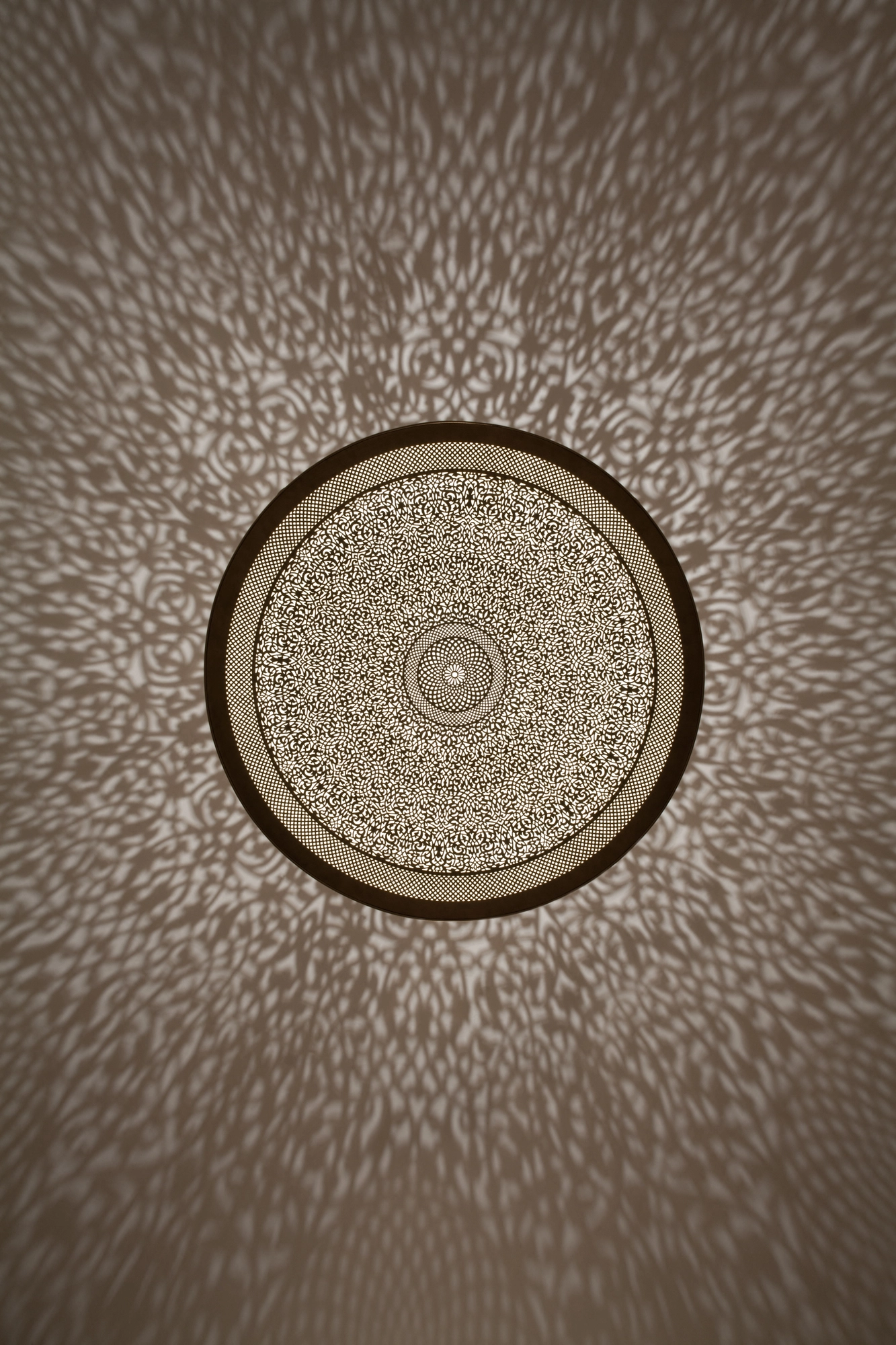 Circular pierced disc-dome ceiling light seen from directly below, ringed by a fine halo of projected light dots.