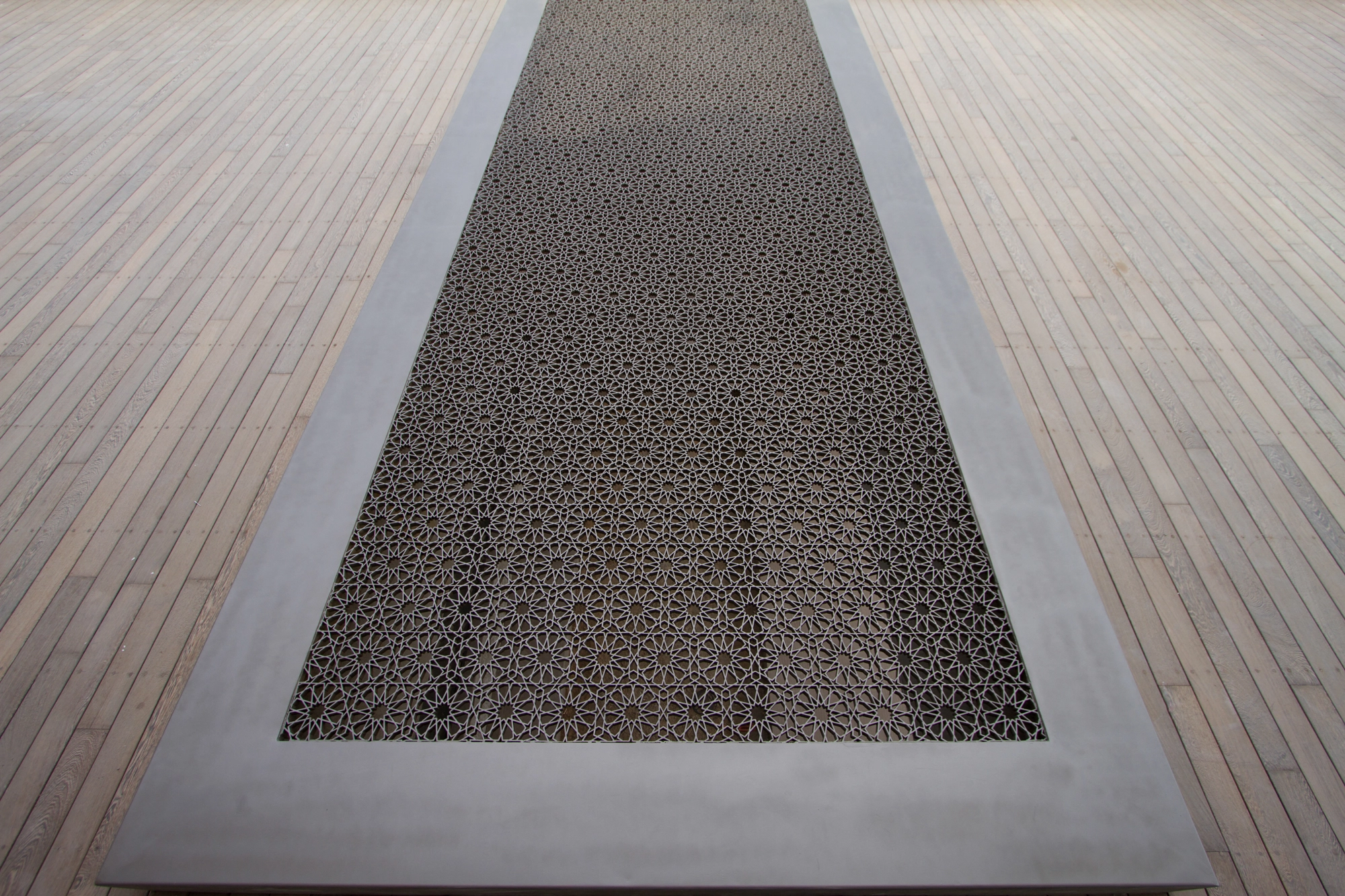 A long rectangular pierced-metal panel set into a pale timber floor as a skylight inset.