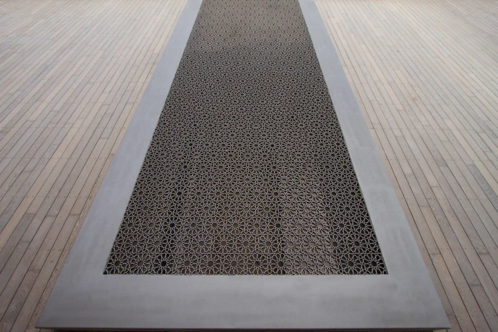 A long rectangular pierced-metal panel set into a pale timber floor as a skylight inset.