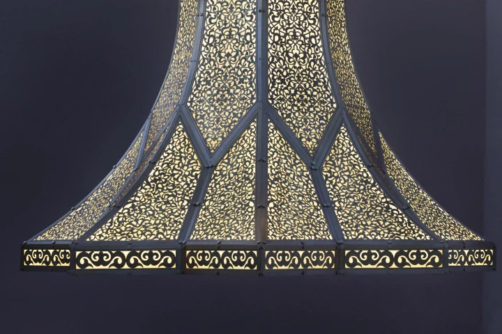 The flared base of the gilded pierced lantern column glowing against dark with an inscribed band, Singularity.