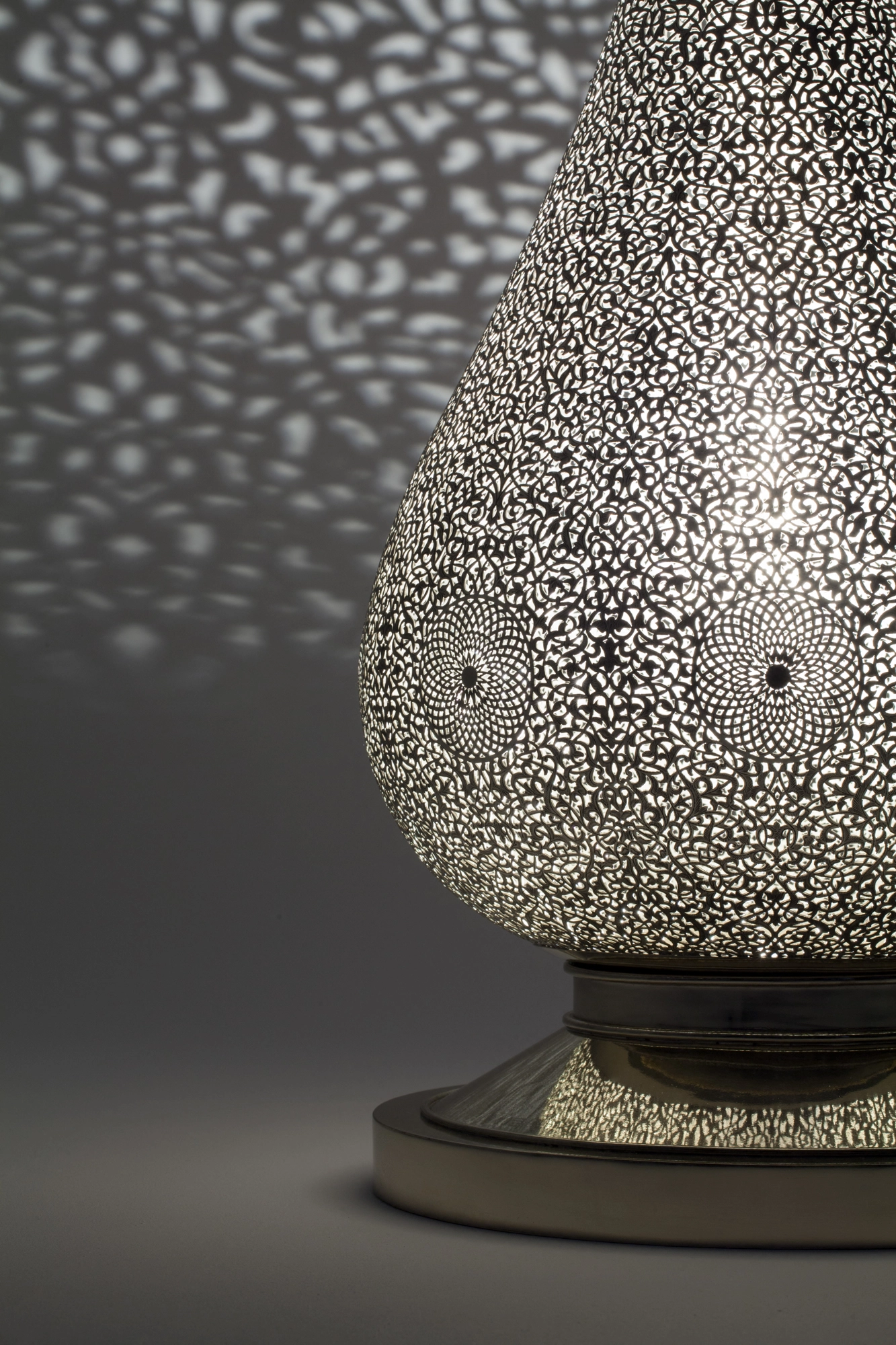 A pierced teardrop floor lamp tilted on its base, scattering a fine dotted spray of light on a grey ground.