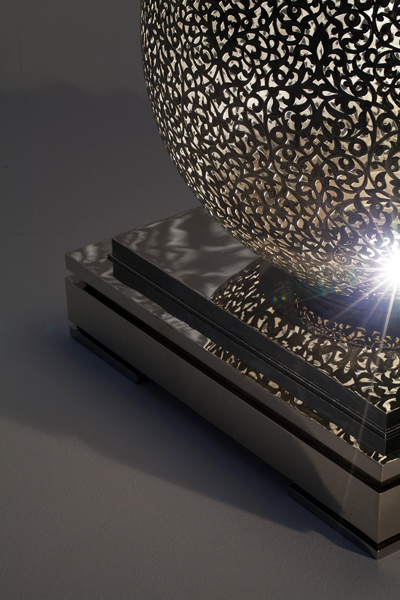 Close-up of a pierced teardrop floor lamp meeting its base, with a bright burst of light at the seam.