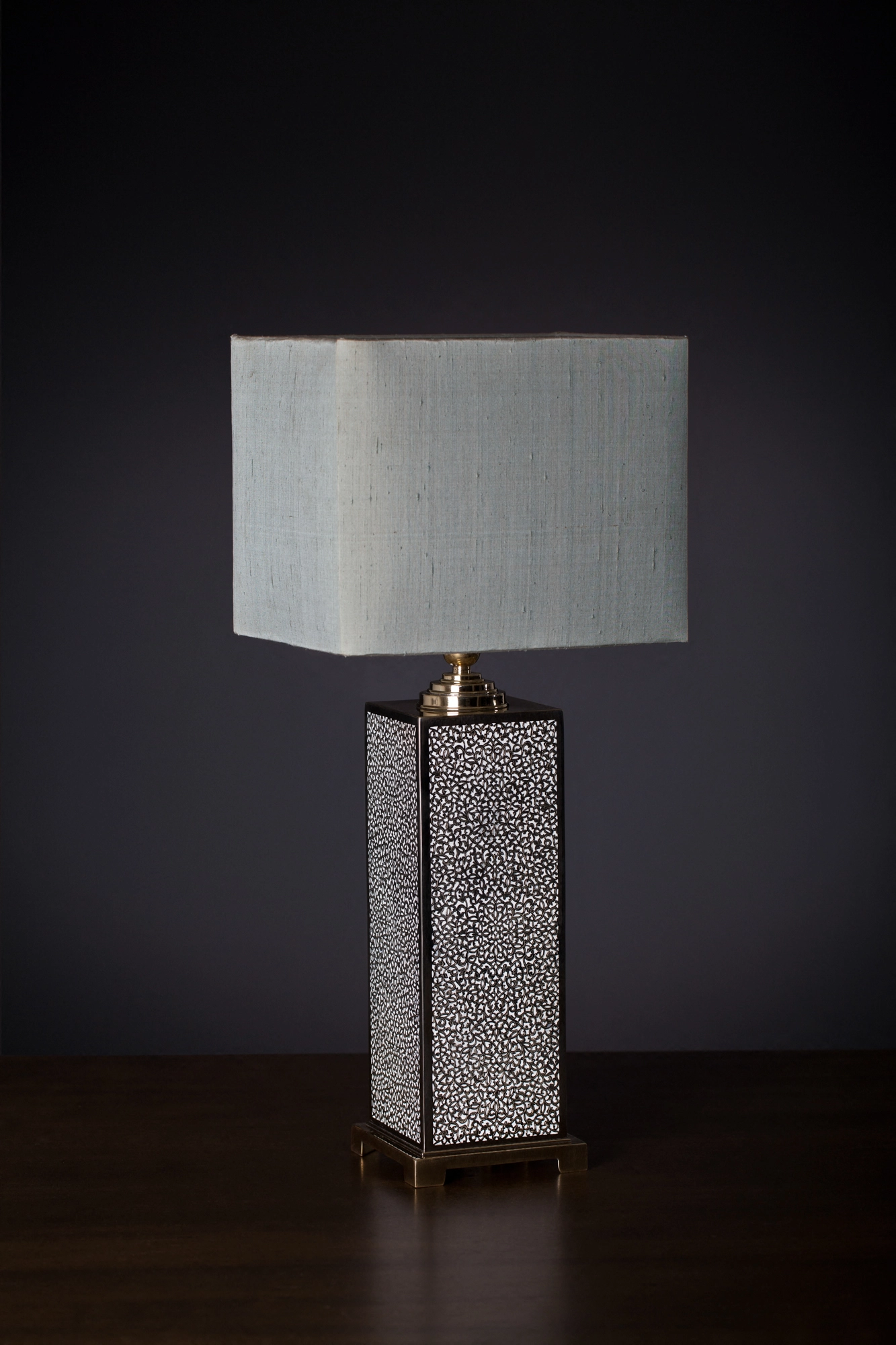 Table lamp with a pierced silver-and-enamel rectangular base and a pale rectangular shade, on a black background.
