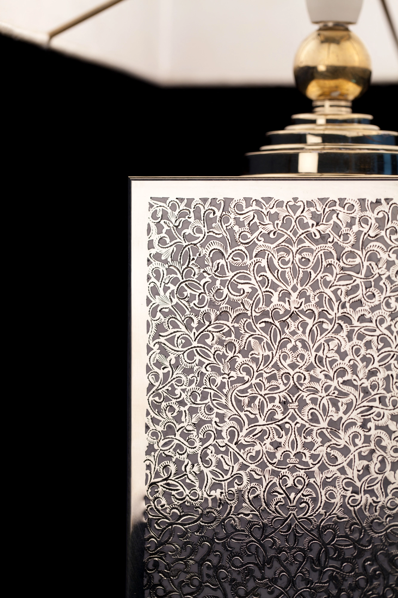 Close-up of a table lamp's hand-sawn floral panel with enamel inlay, lit to reveal fine pierced detail.