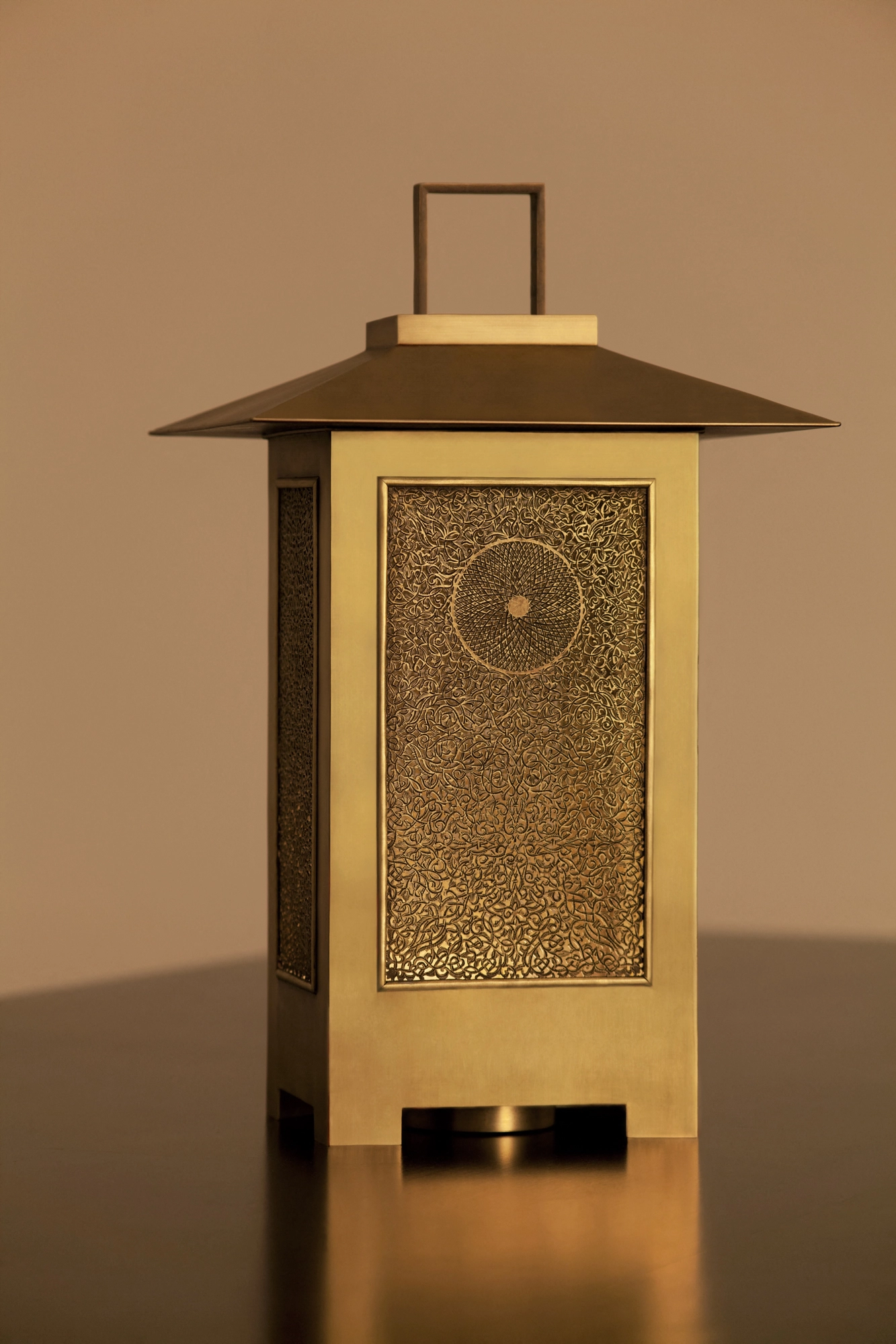 A brass lantern with a pagoda-style roof and a floral pierced panel, glowing warmly on a reflective surface.