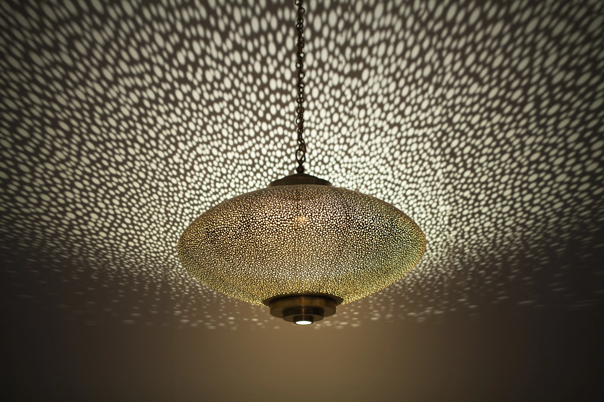 Pierced-silver squashed-globe pendant on a cord, casting a soft halo of light dots across the ceiling.