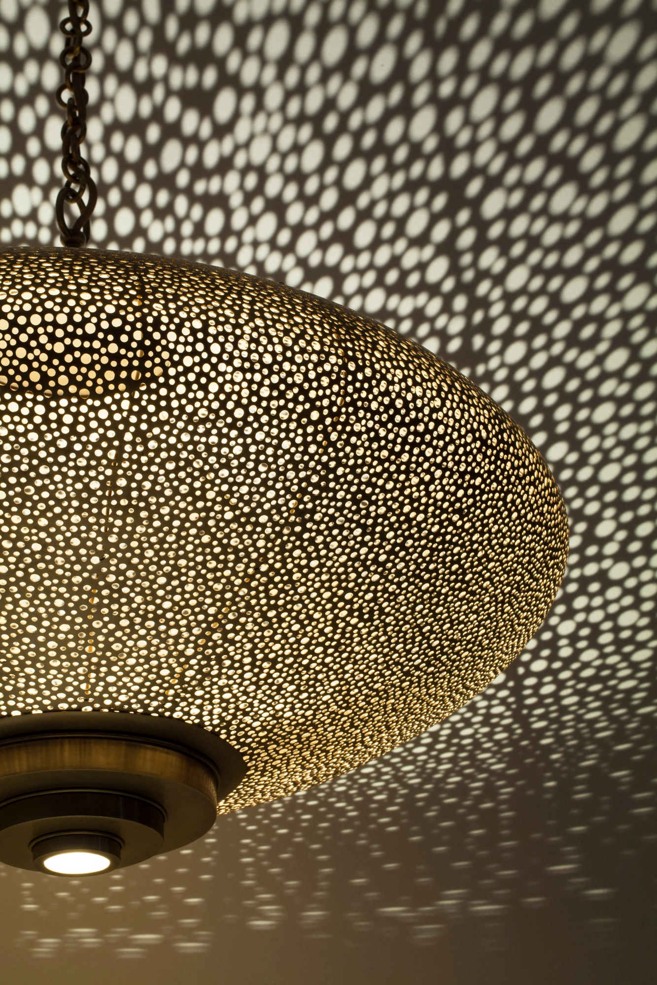 Underside close-up of a pierced squashed-globe pendant, its dense perforations scattering light across the ceiling.