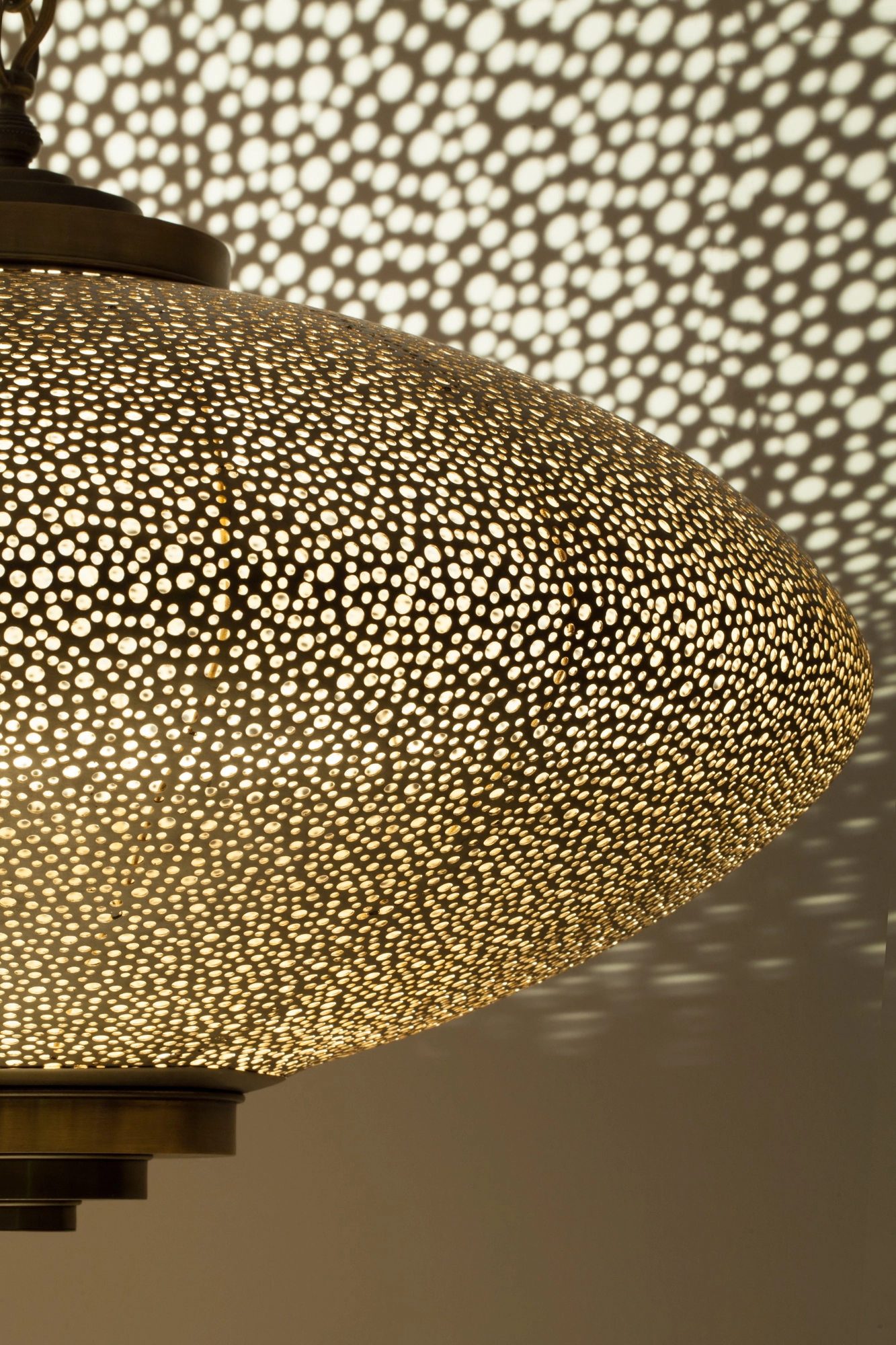 Close-up of a pierced squashed-globe pendant lit from within, surrounded by a dense field of projected light dots.