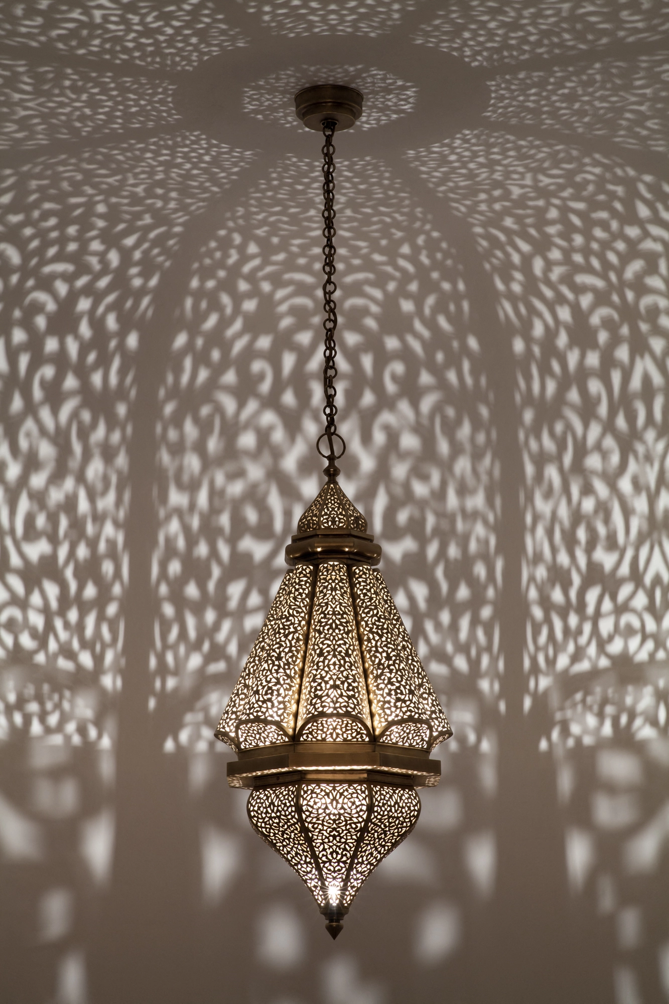 A pierced lantern pendant on a chain casting arched patterns of dotted light across the walls.