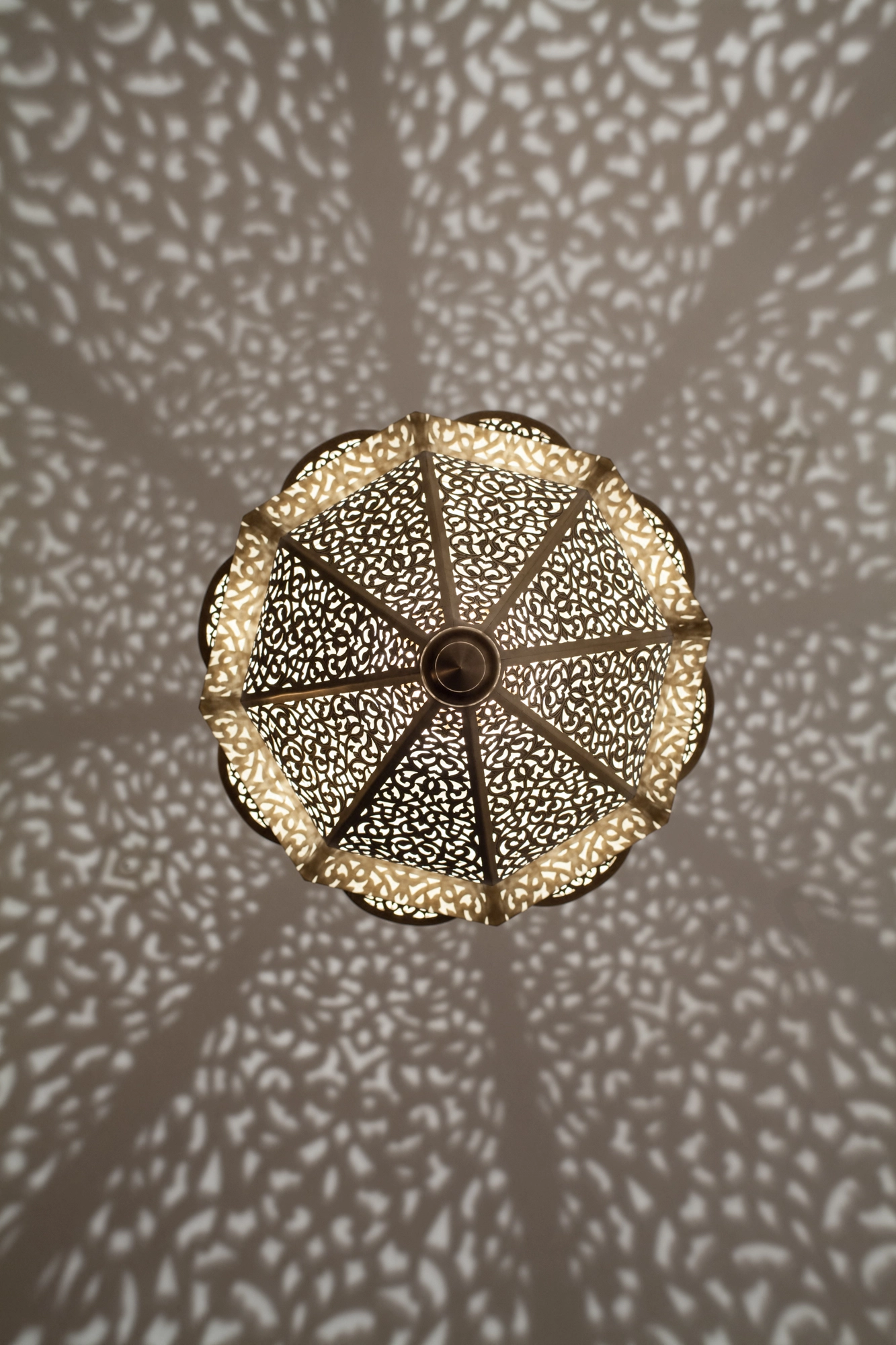 A pierced lantern pendant viewed from directly below, radiating a spoked spray of dotted light.