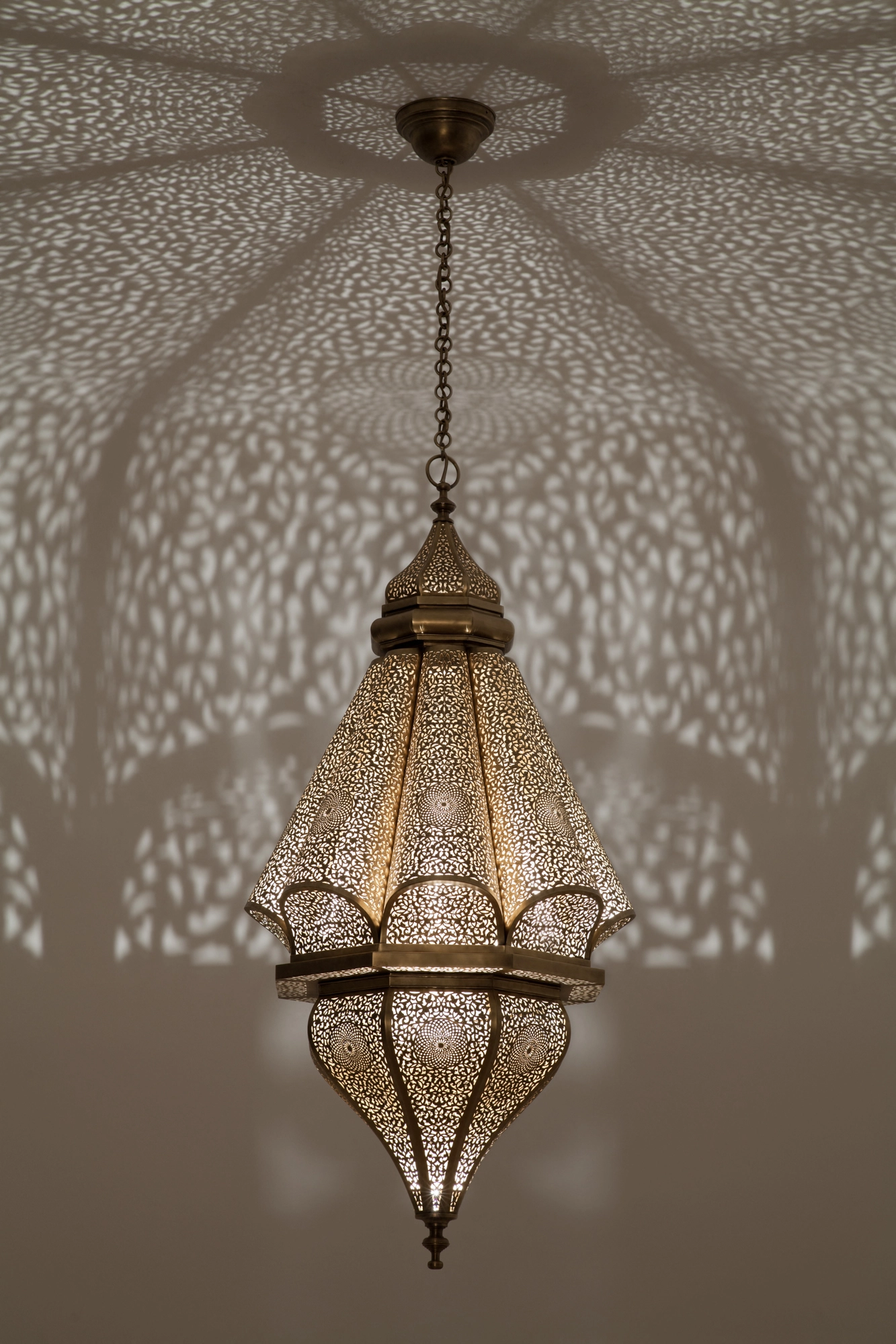 A pierced lantern pendant with a crown-like top on a chain, scattering dotted light across the ceiling.