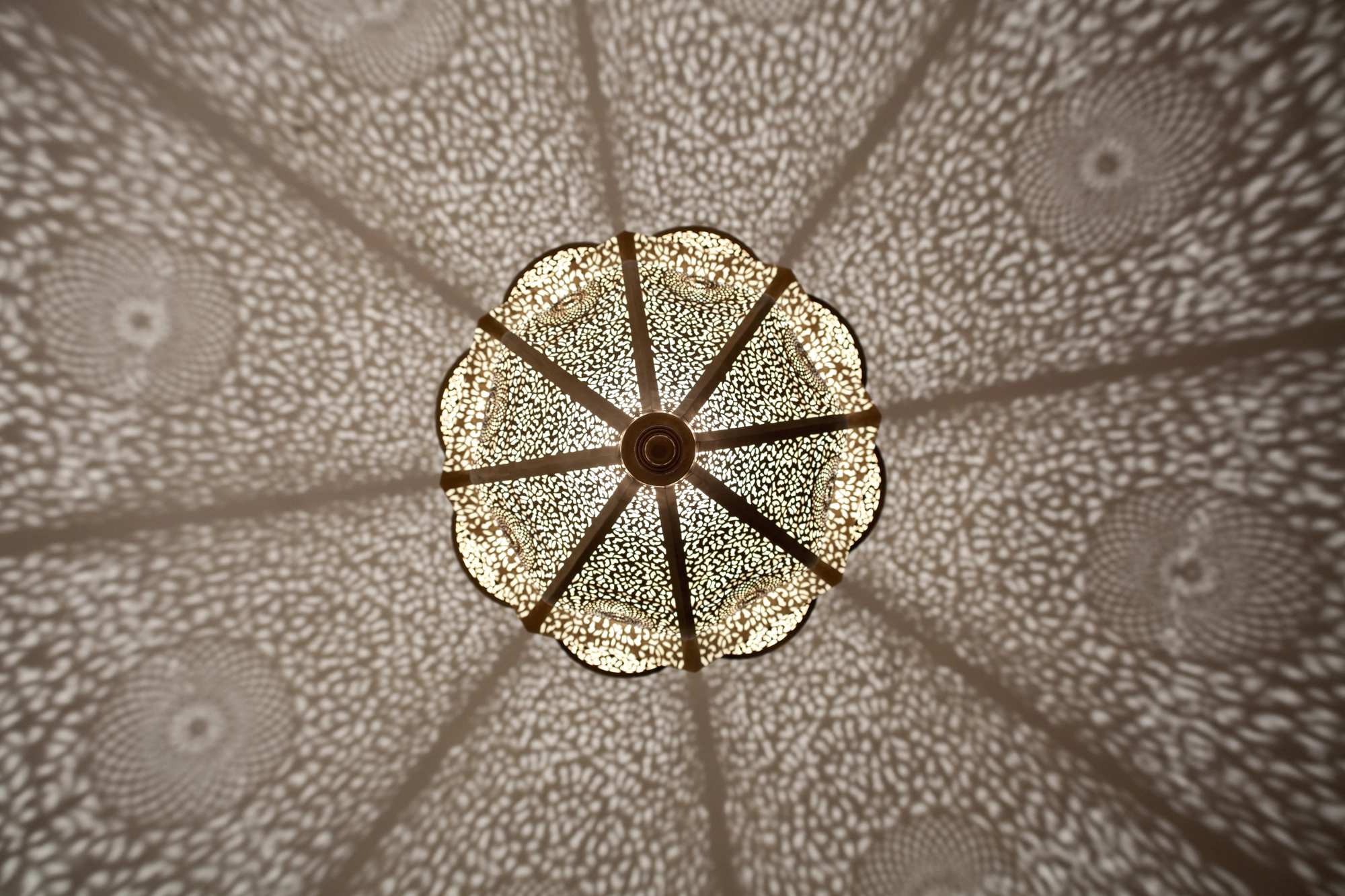 A pierced lantern pendant seen from below, its octagonal frame radiating dotted light outward.