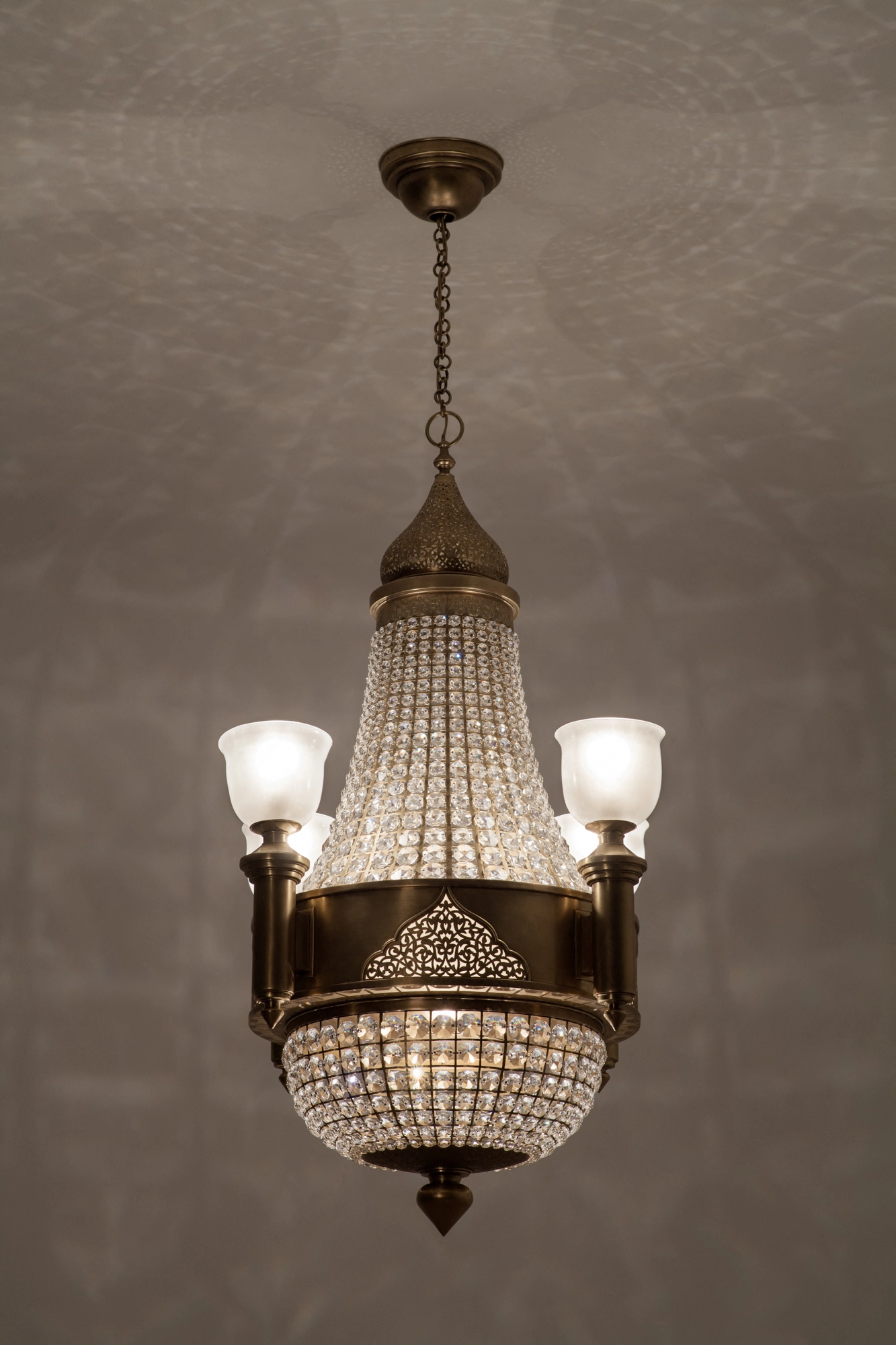 A crystal basket chandelier with four frosted-glass uplights on a brass frame, hung from the ceiling.
