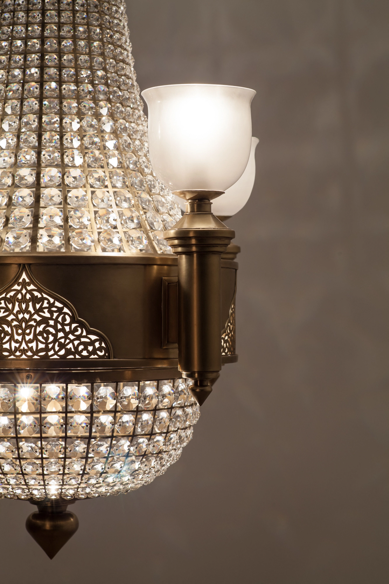 Close-up of a crystal chandelier's beaded tiers, a frosted-glass uplight and a pierced brass band.