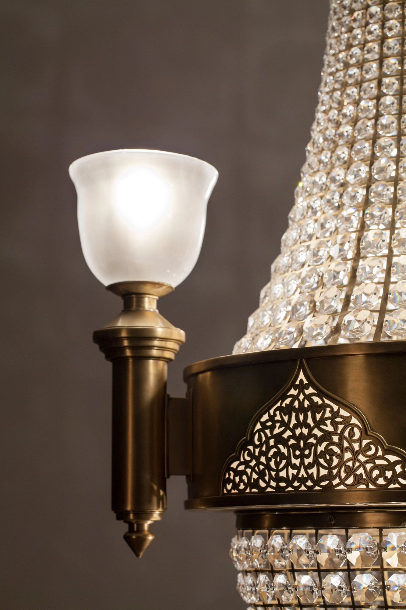 Close-up of a chandelier's frosted-glass uplight cup on a brass arm beside crystal beading.