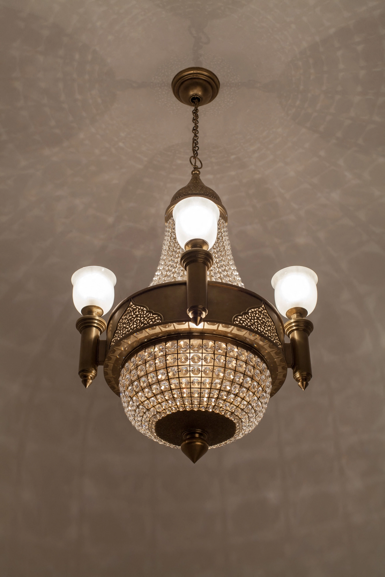 A crystal basket chandelier with frosted uplights seen from a low angle against a grey ceiling.
