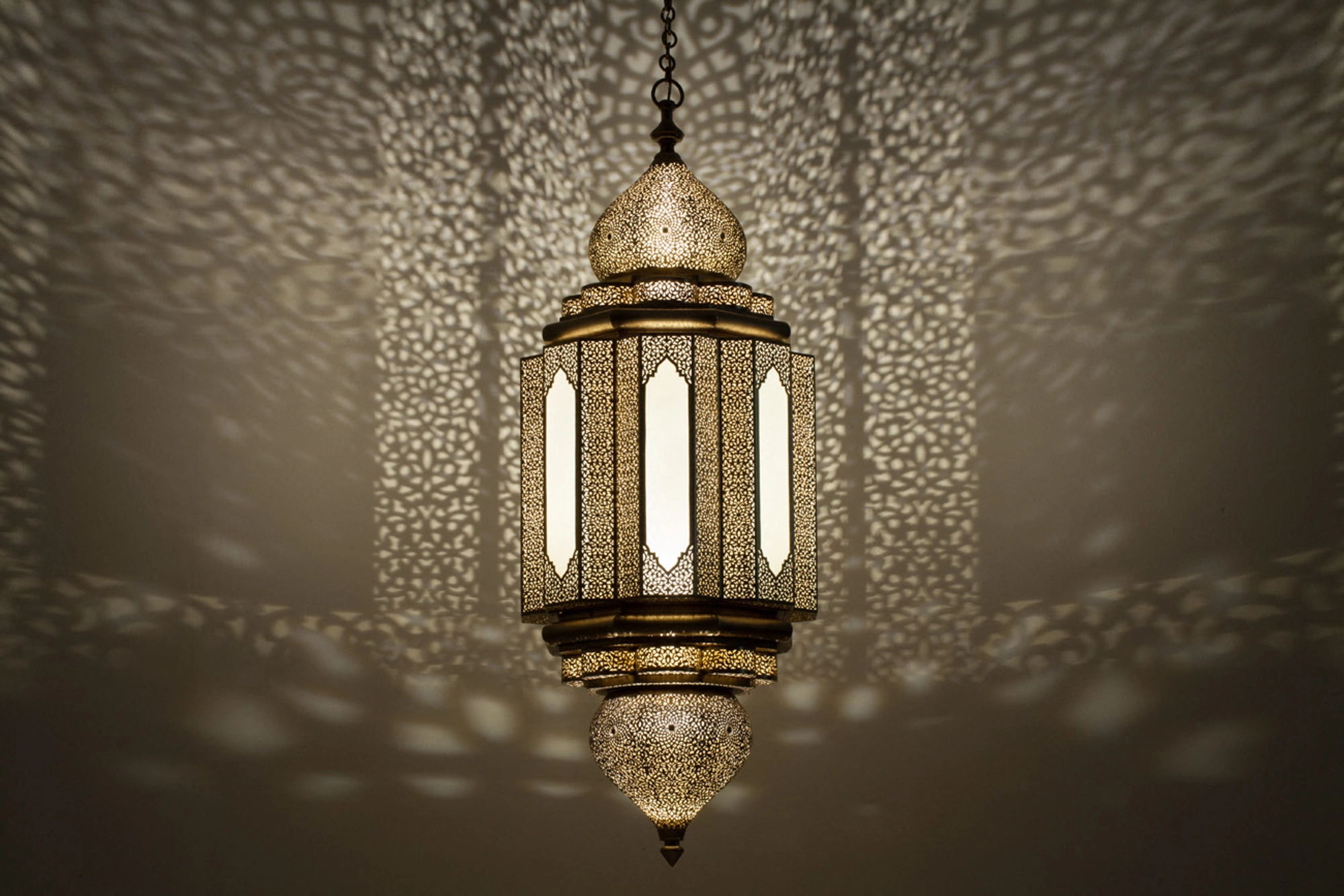 A Moorish lantern with frosted glass panels and a pierced metal dome, glowing softly in a dim room.