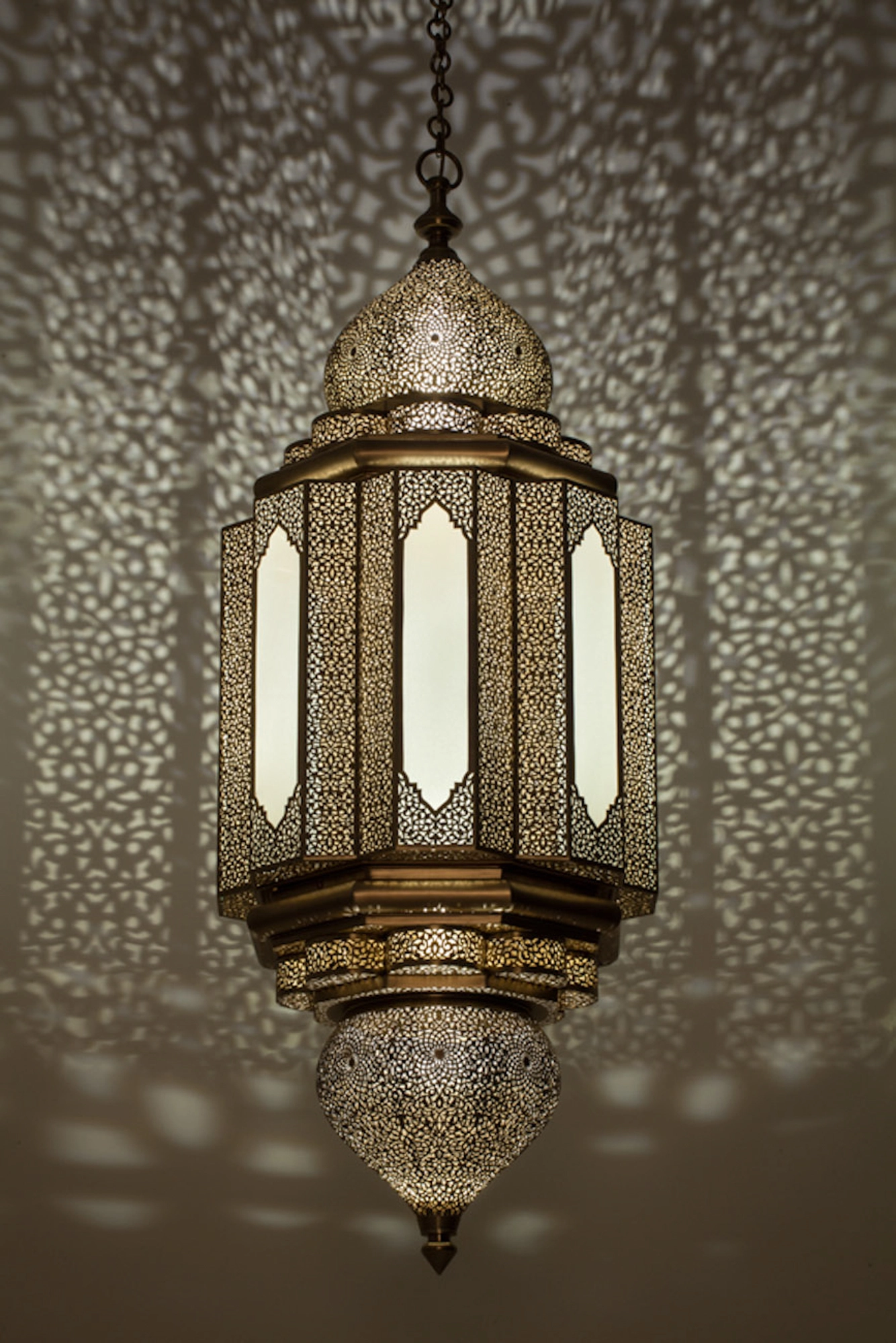 A hexagonal Moorish lantern with frosted glass panels and a pierced dome, scattering dotted light around it.