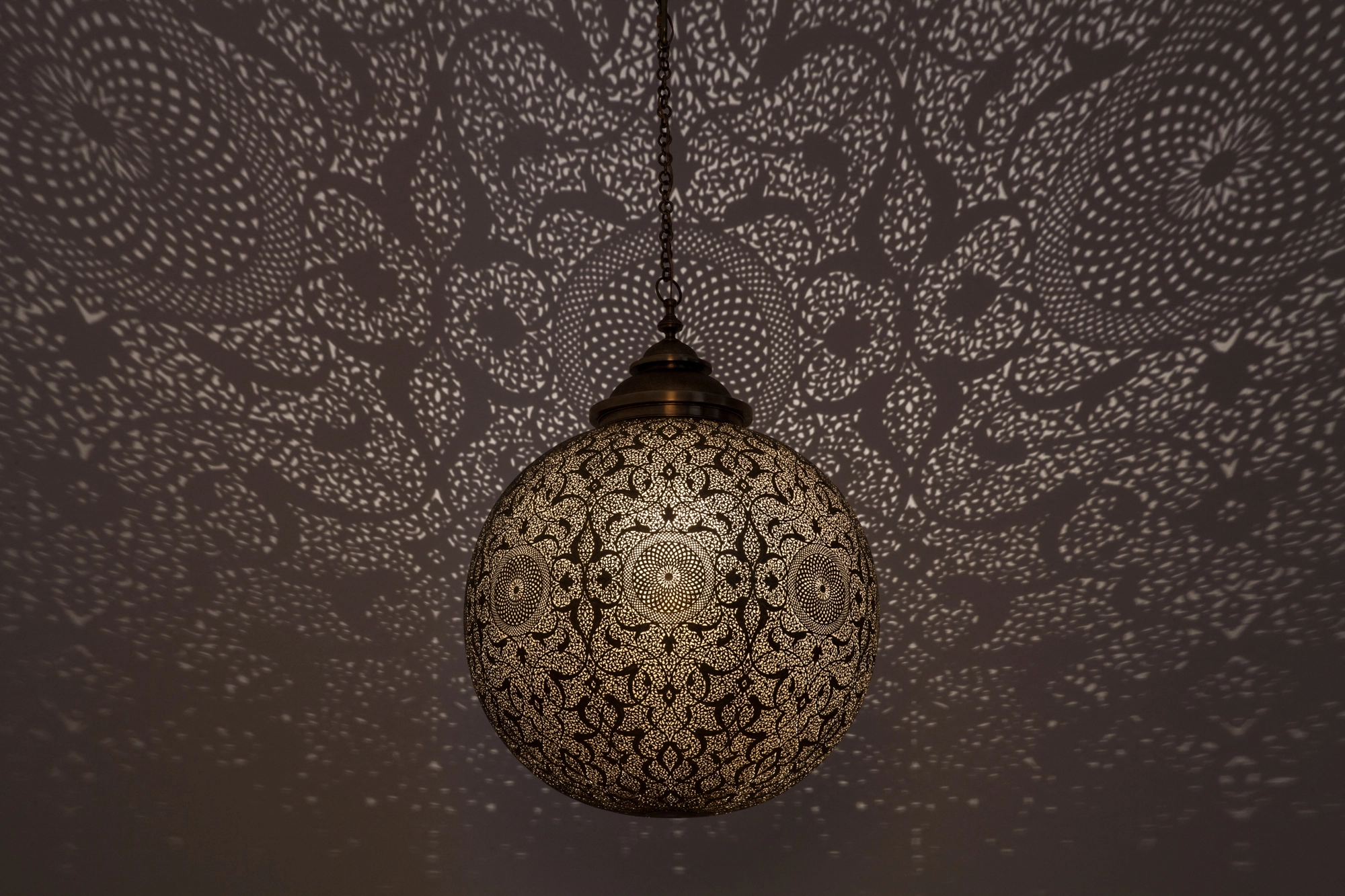 A pierced brass globe pendant lamp casting a dense foliage-like pattern of shadow across the ceiling.