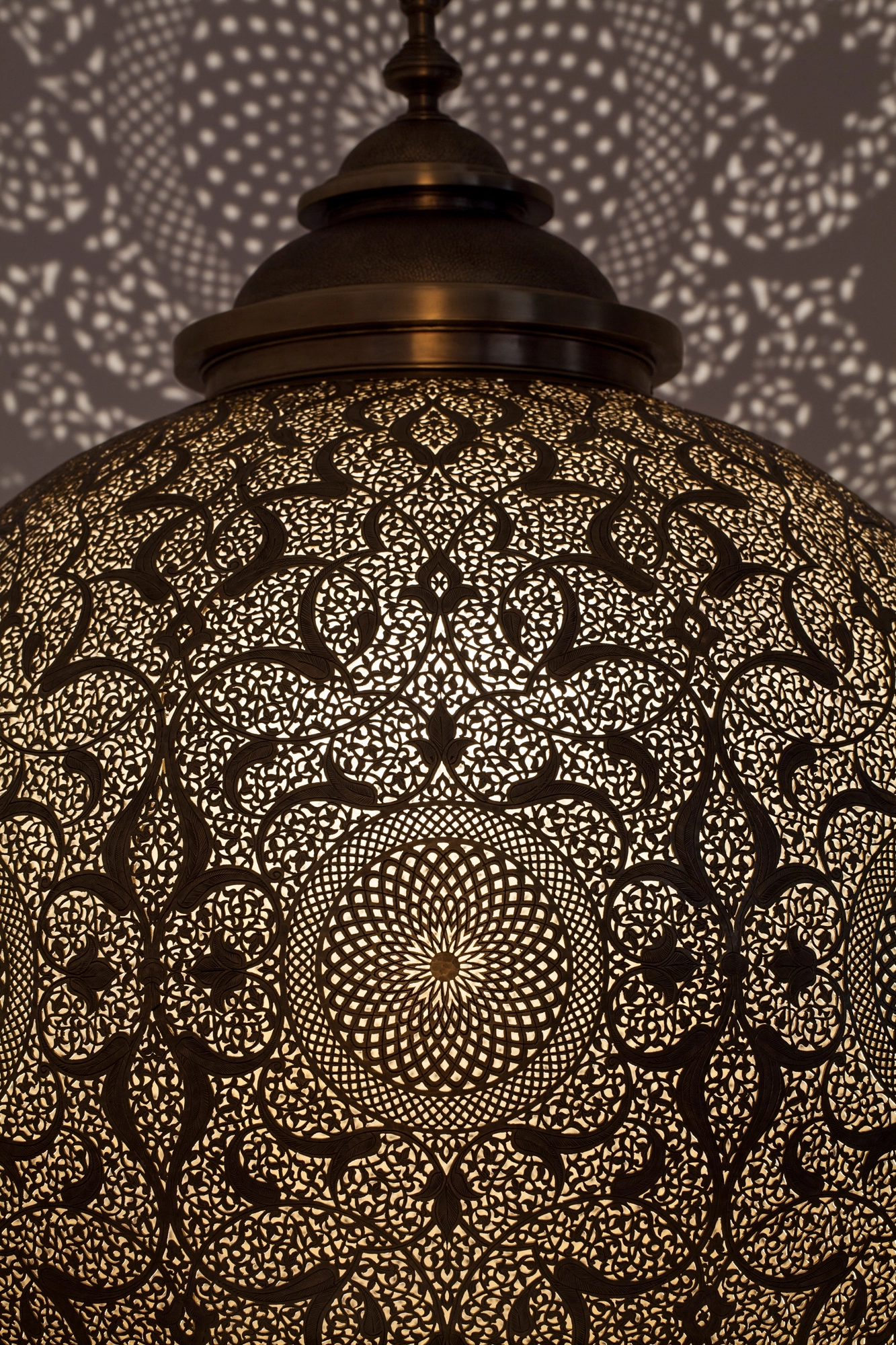 Close-up of a pierced brass globe pendant lamp glowing with a radiating star-burst pattern.