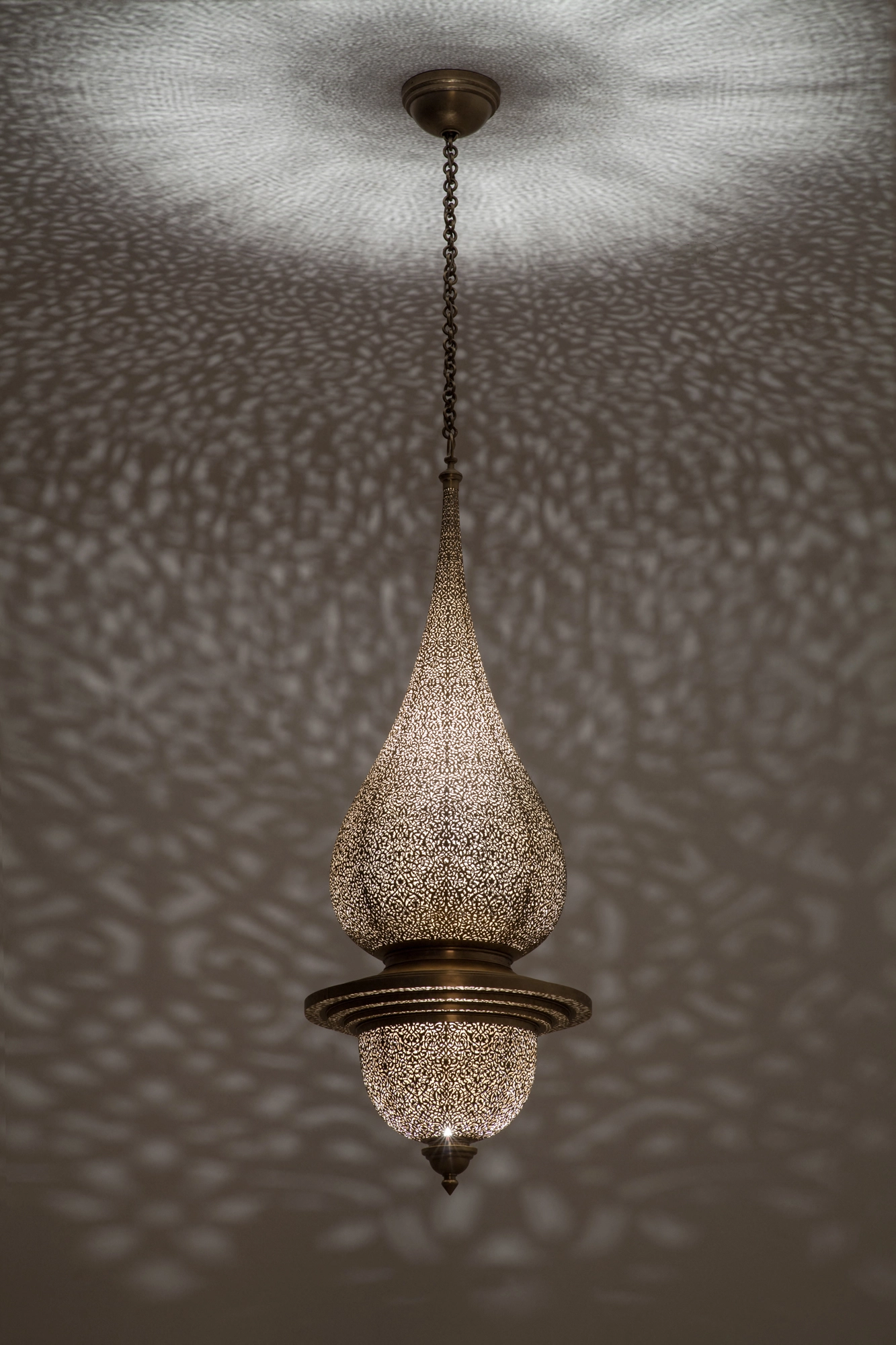 A pierced teardrop pendant lamp on a long chain, scattering a fine dotted glow across the ceiling.