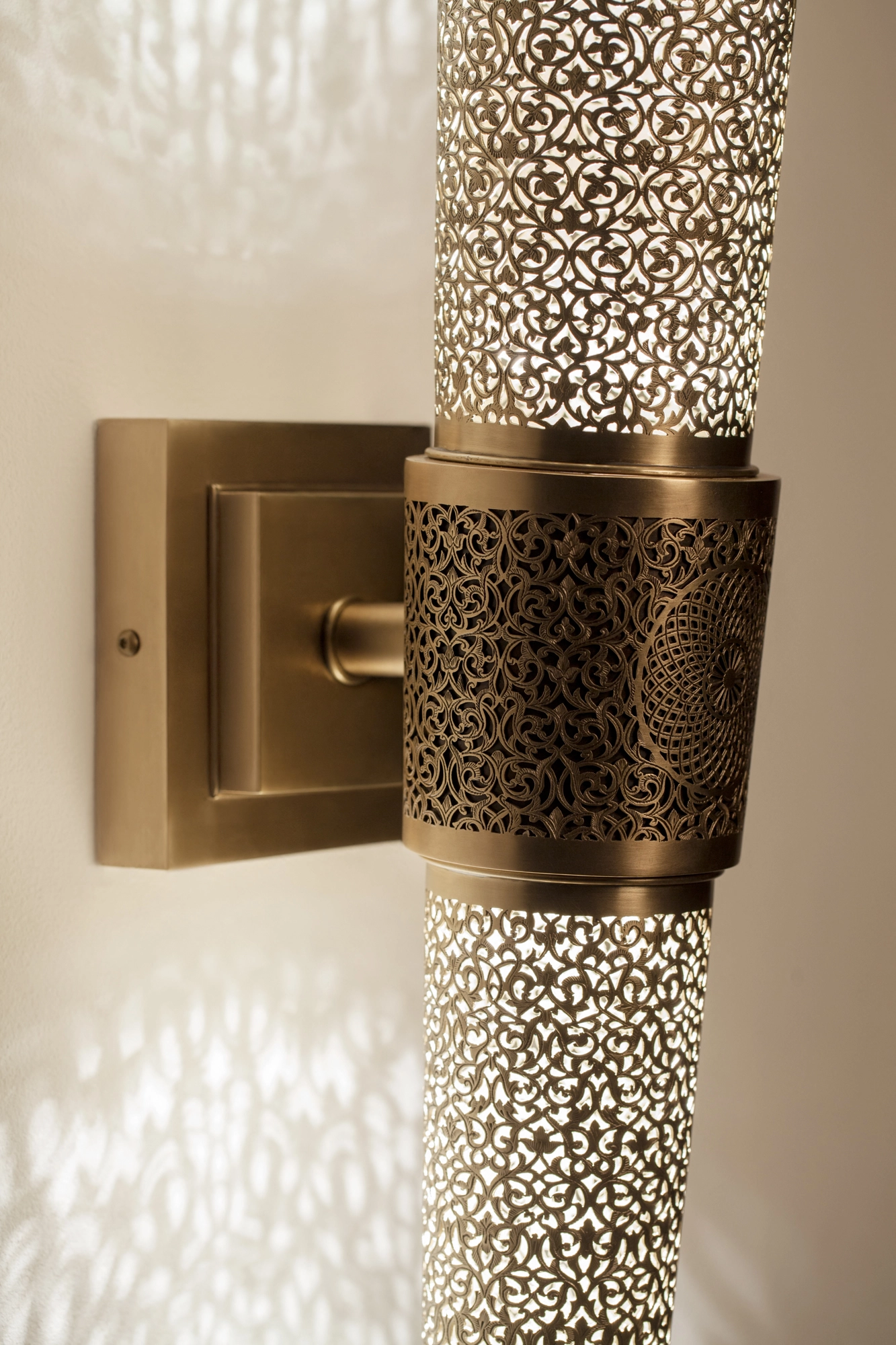 Close-up of a torch wall light's brass bracket gripping a pierced cylinder, set against a lacy light pattern.