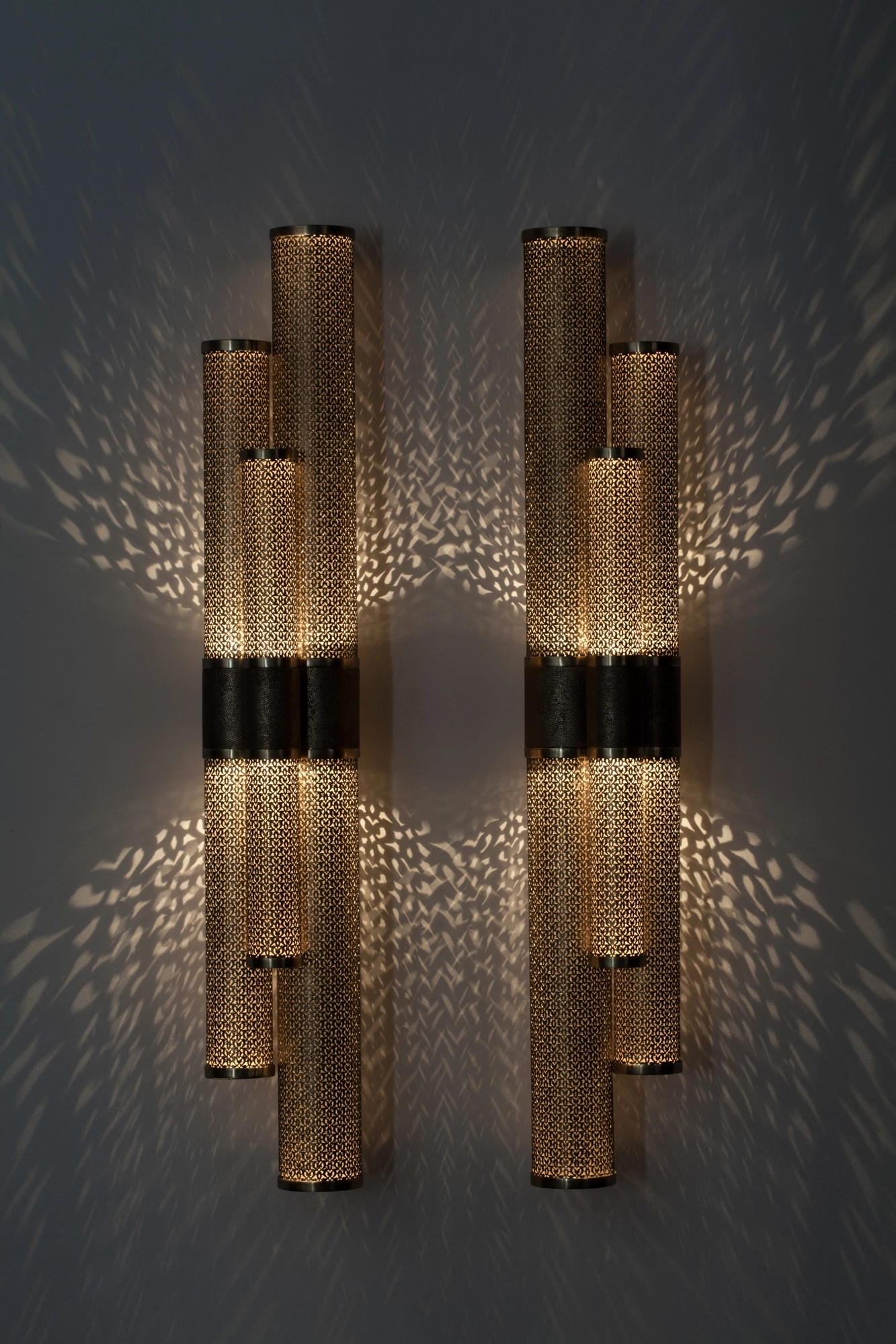 Two clusters of pierced-brass triple cylinders mounted side by side, glowing with feathery light bursts.