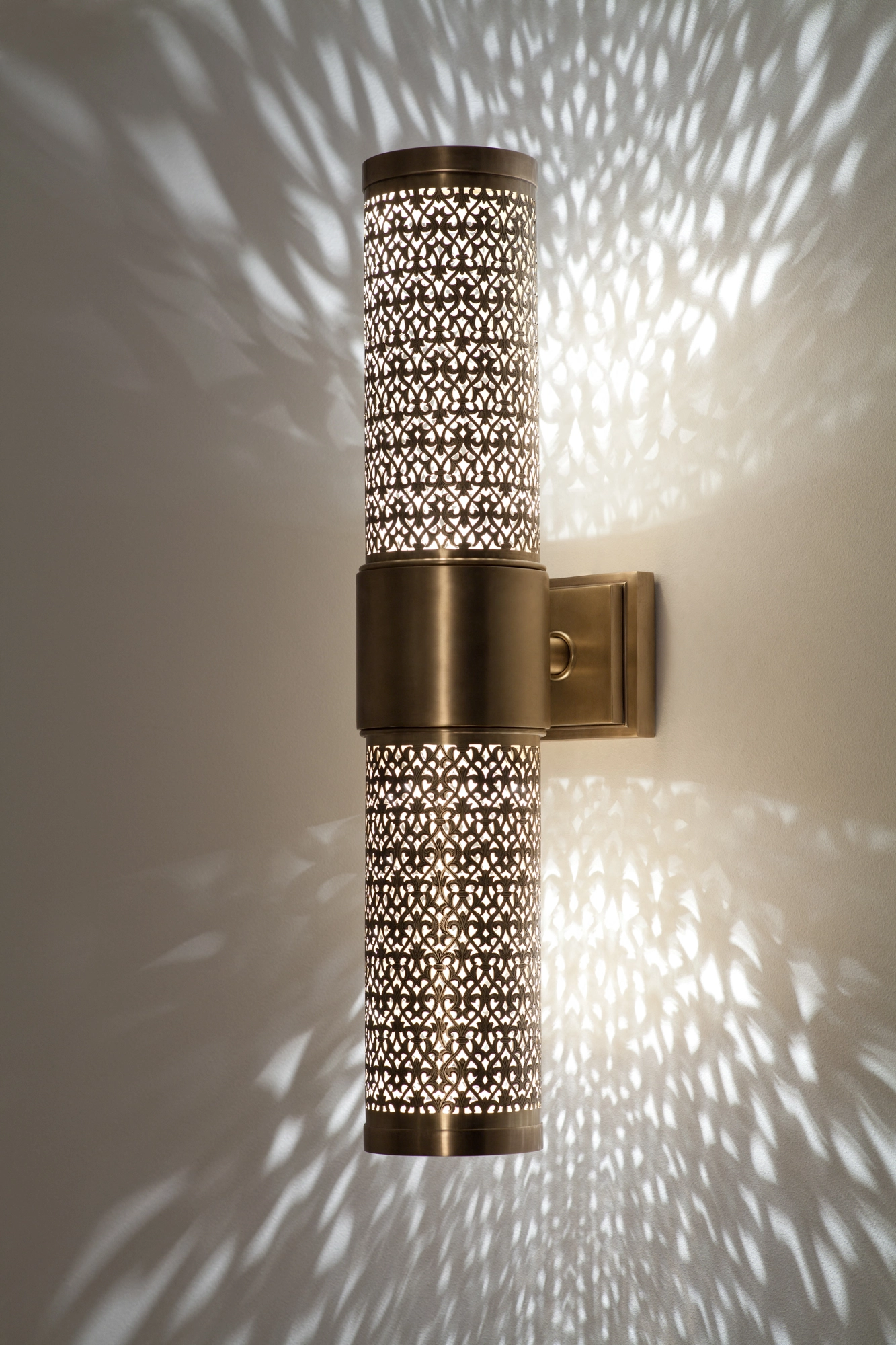 Single tall pierced-brass cylinder wall light on a bracket, glowing amid a wide scatter of light dots.