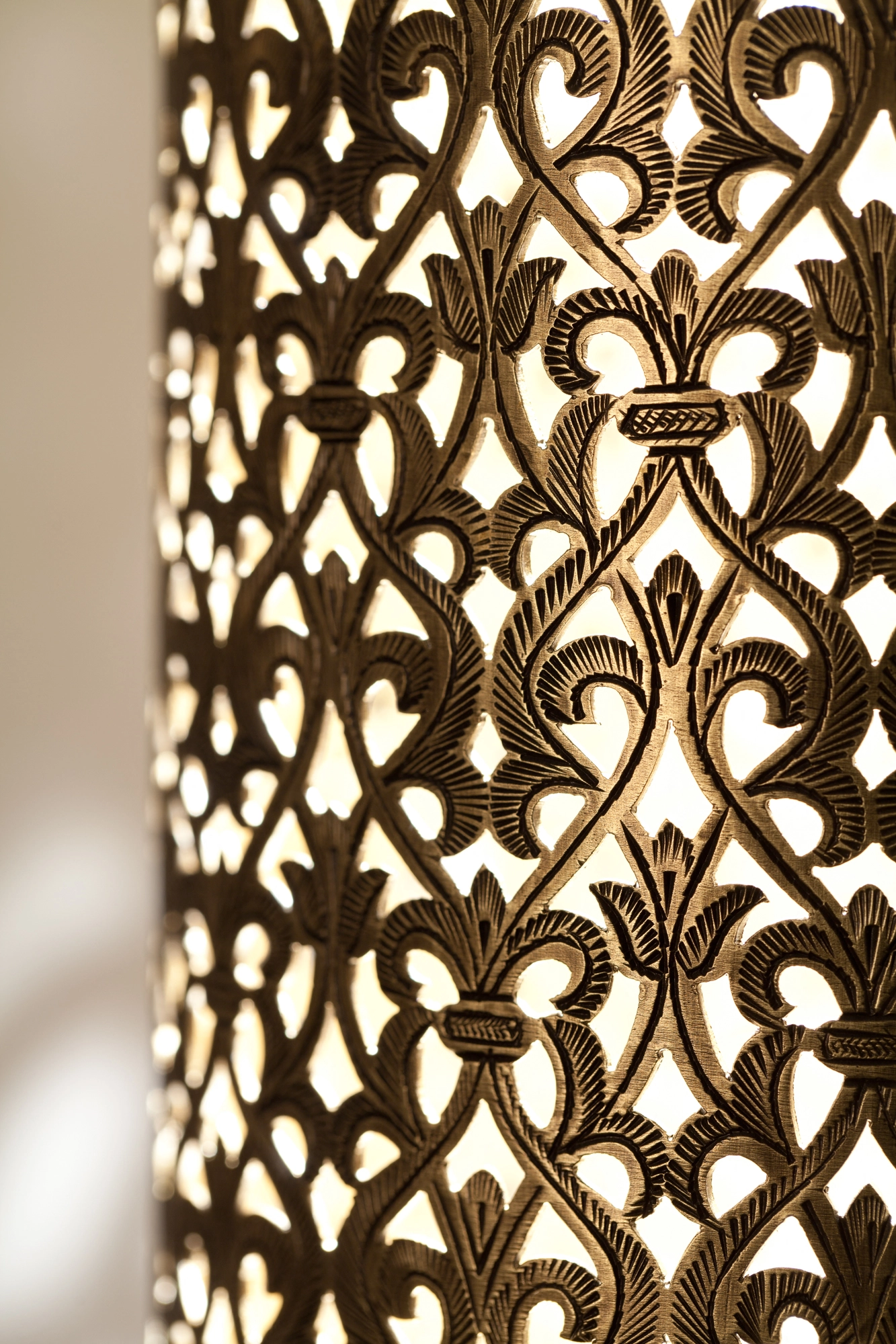 Close-up of a wall light's pierced-brass surface, its floral fretwork glowing warm against shadow.