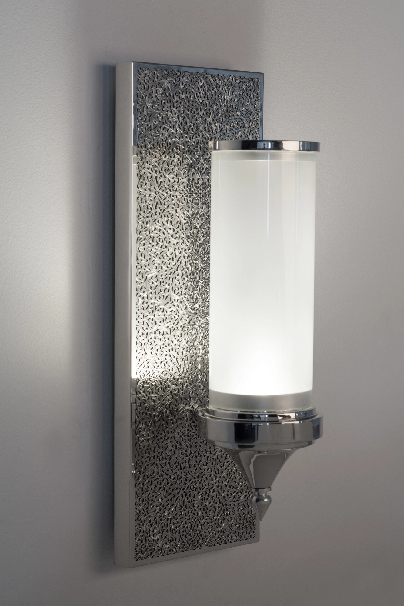 Wall sconce with a white glass cylinder mounted on a hammered-silver square backplate.