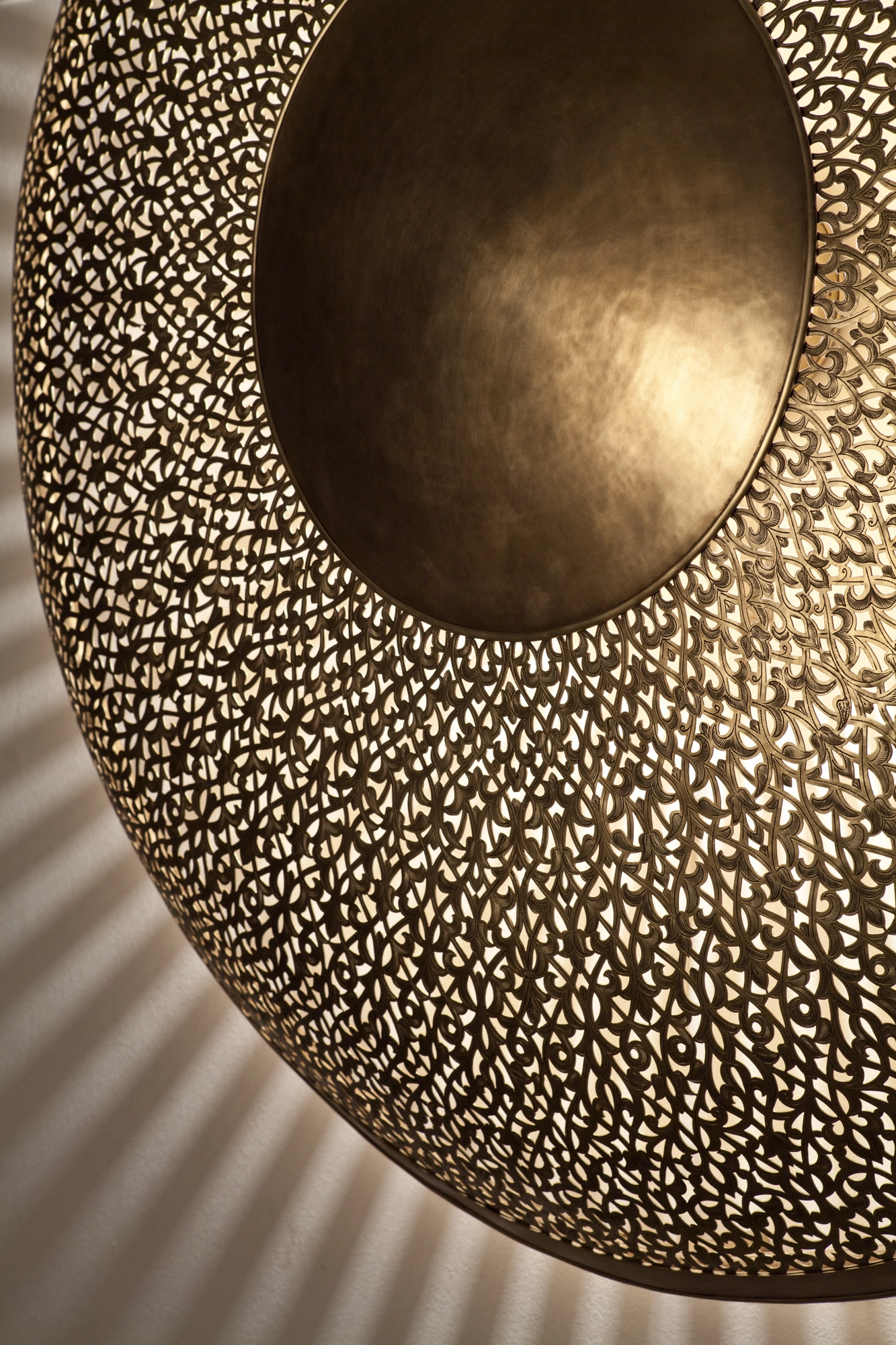 Angled close-up of a pierced-brass sunburst wall light, its domed center rising from a dense perforated disc.