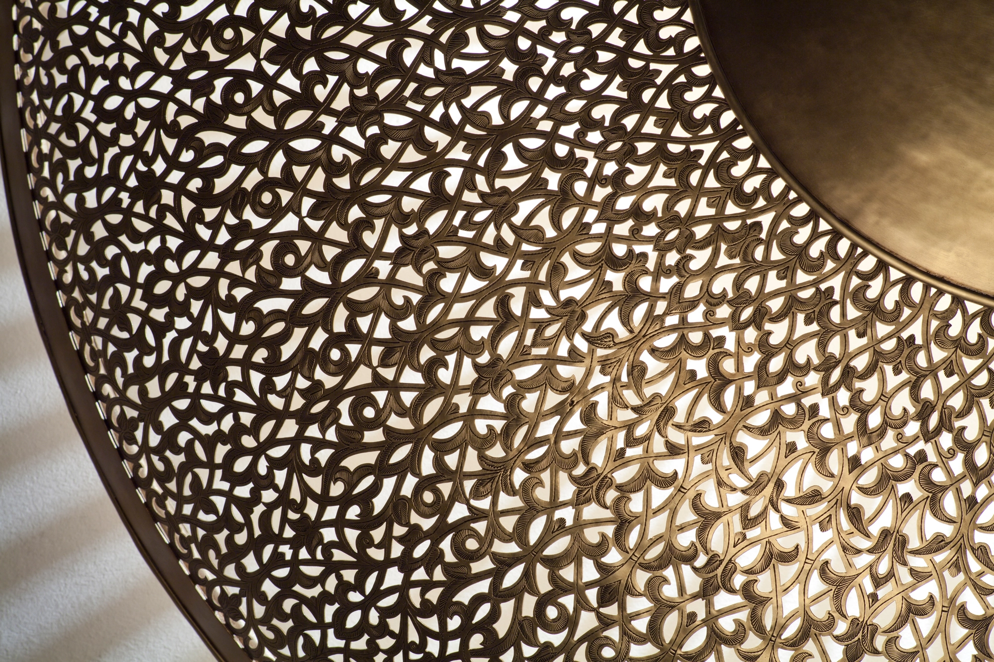 Close-up of a pierced-brass sunburst disc, its fine perforations glowing warm along the curved edge.