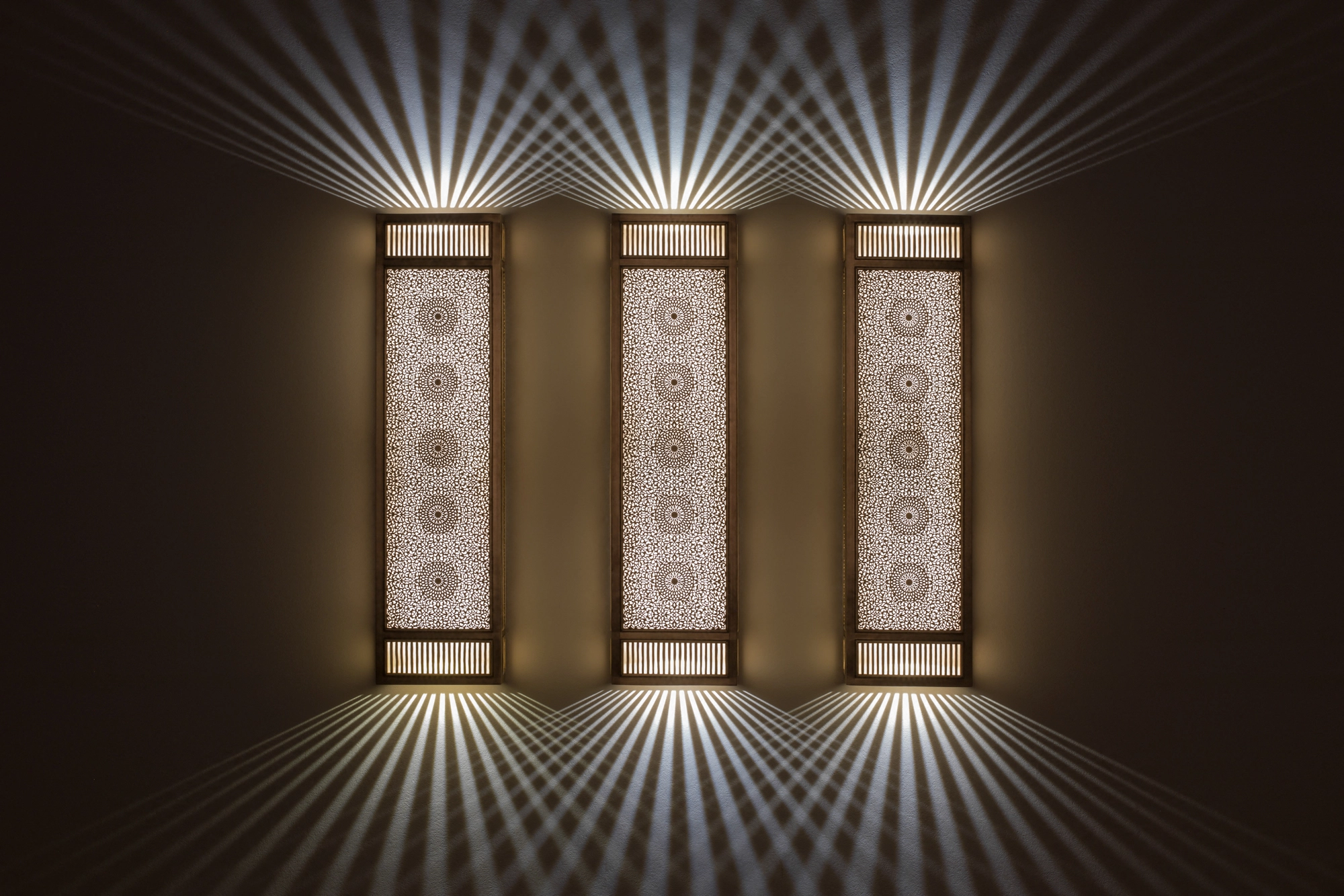 Three pierced-brass rectangular box wall lights in a row, glowing and casting up-and-down fans of light.