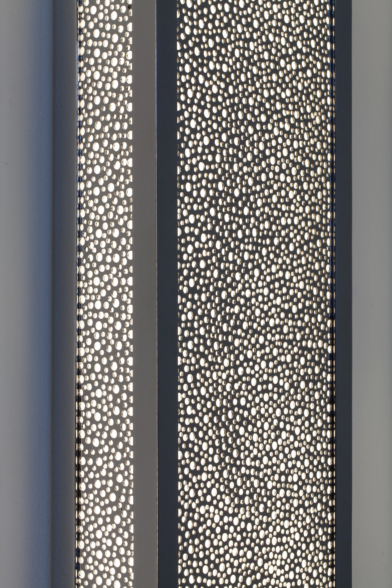 Close-up of two pierced-brass rectangular panels with dense dotted fretwork, lit side by side.