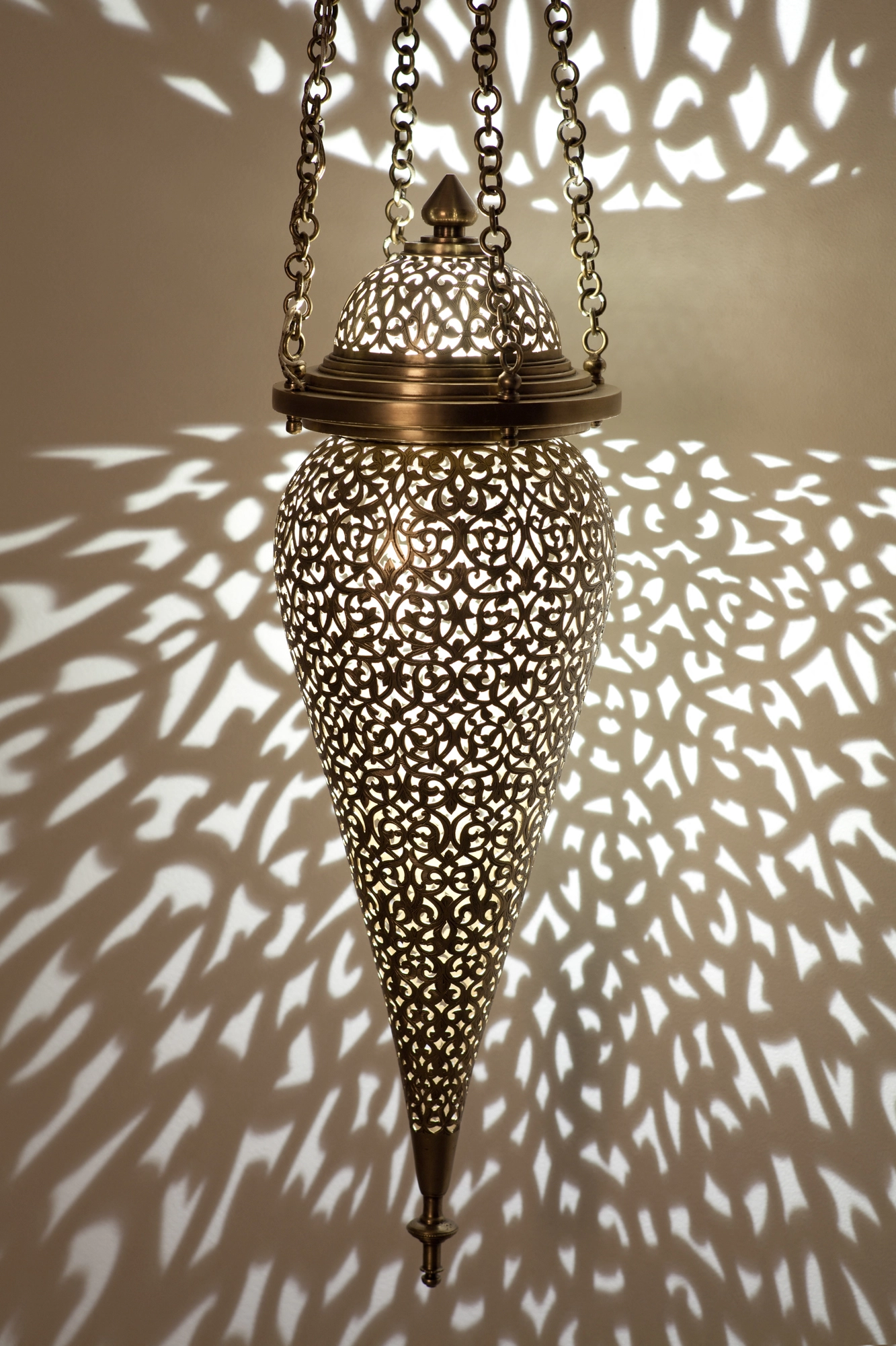 Pierced-brass tear-drop lantern suspended on chains, casting a dense field of light dots across the wall.