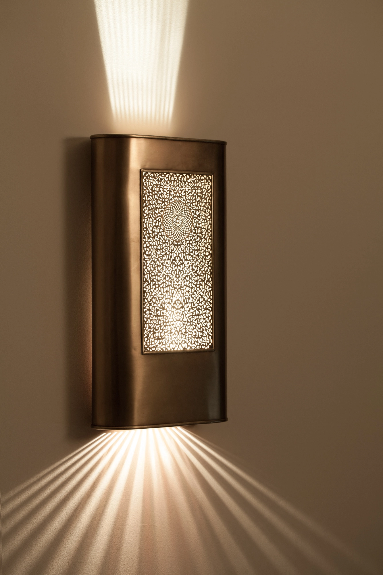 Curved brass tube-ovale wall light with a pierced oval panel, casting a cone of light upward and a fan downward.